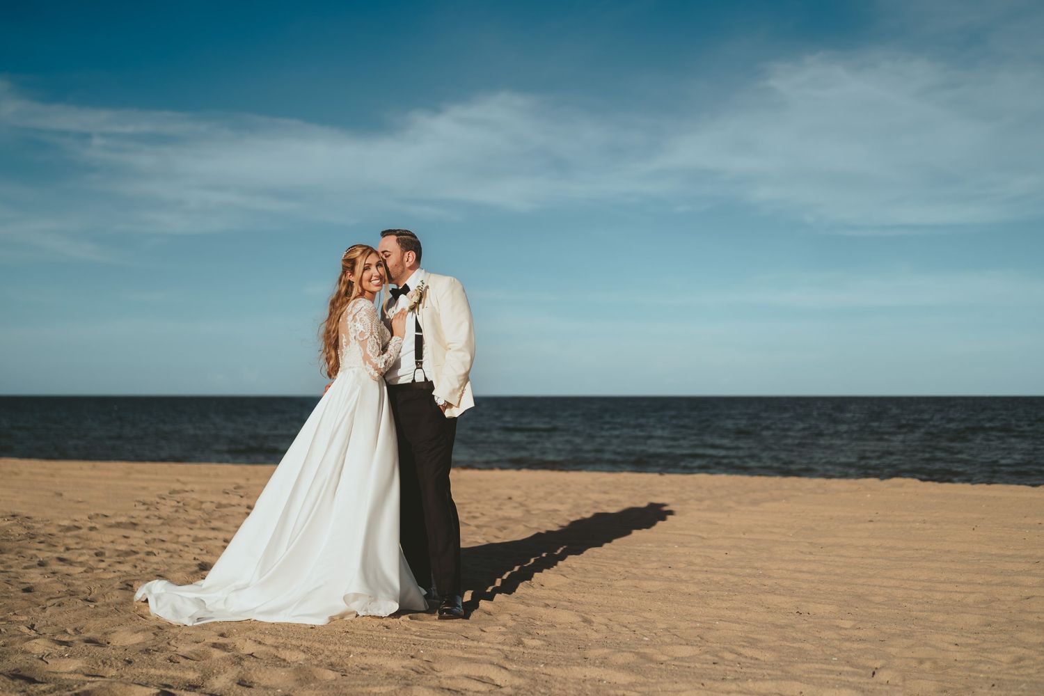 Romántico beso de novios en la playa de Miami al atardecer con el mar y el cielo azul. Fotografía de boda.
