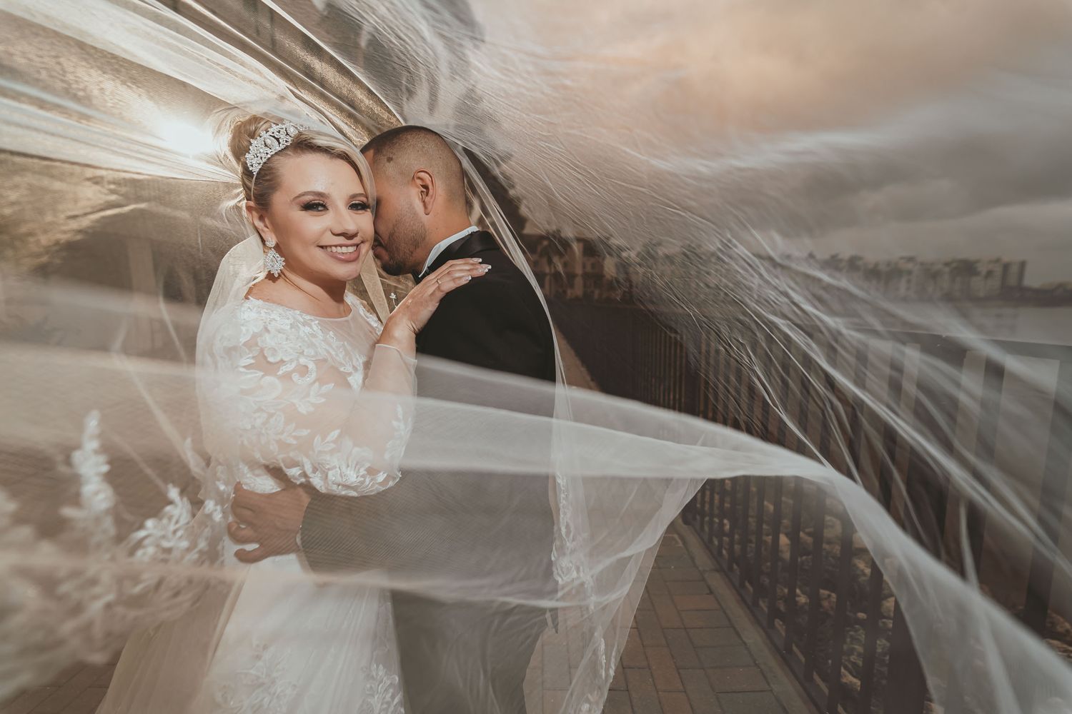 Retrato romántico: Novios posan abrazados bajo el velo flotante de la novia; mirada íntima. Boda en Miami.