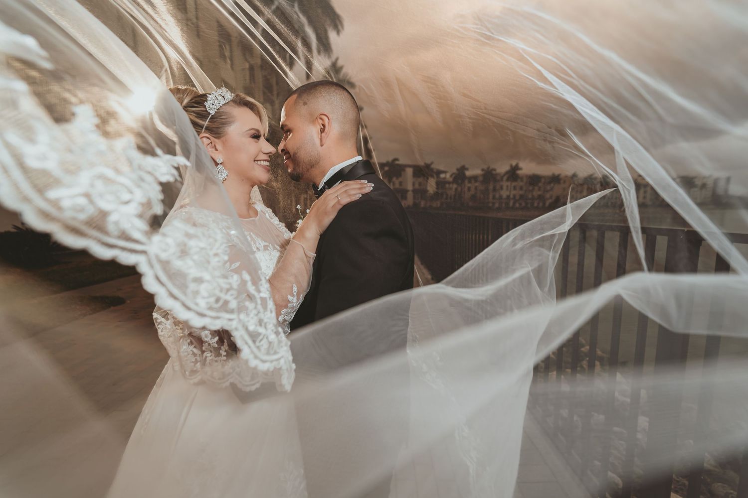 Novios se abrazan y miran bajo el velo transparente de la novia; retrato romántico boda destino en Miami.
