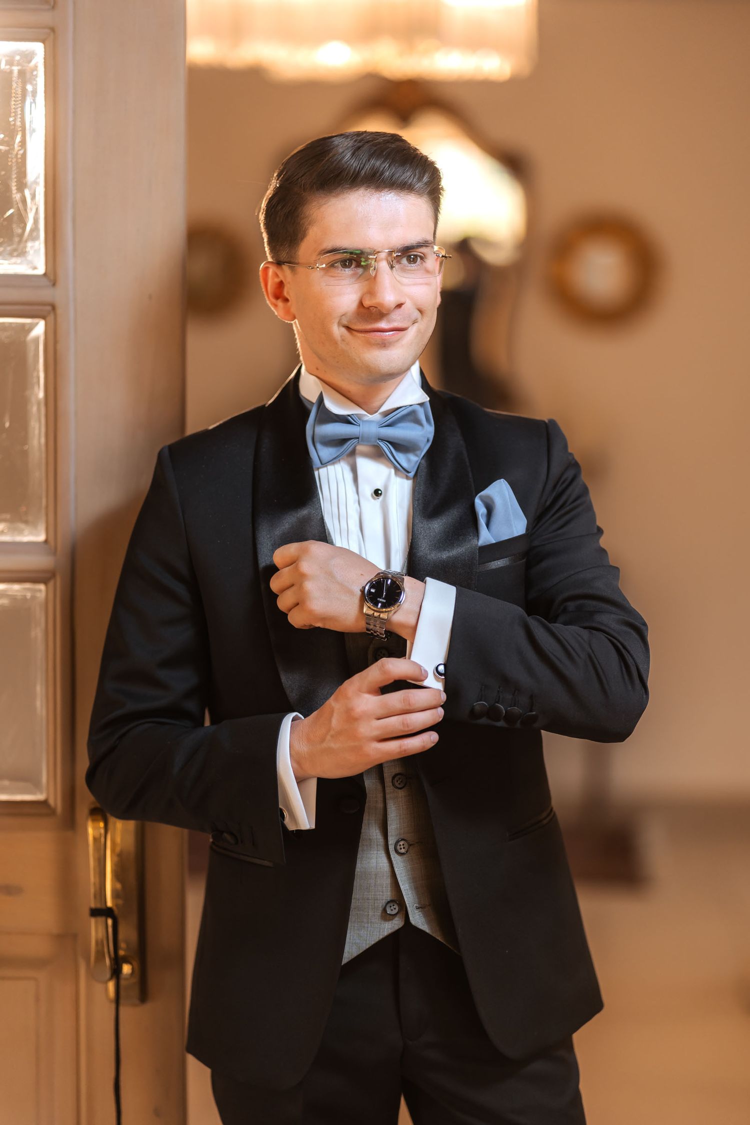 Novio elegante con esmoquin y pajarita azul ajusta su reloj o gemelo en interior; preparación de boda.