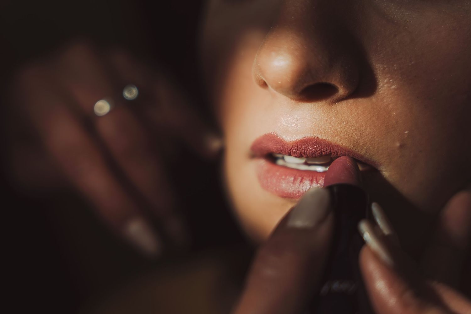 Primer plano: Mano aplicando labial en labios con luz y sombra dramáticas. Preparación de maquillaje.