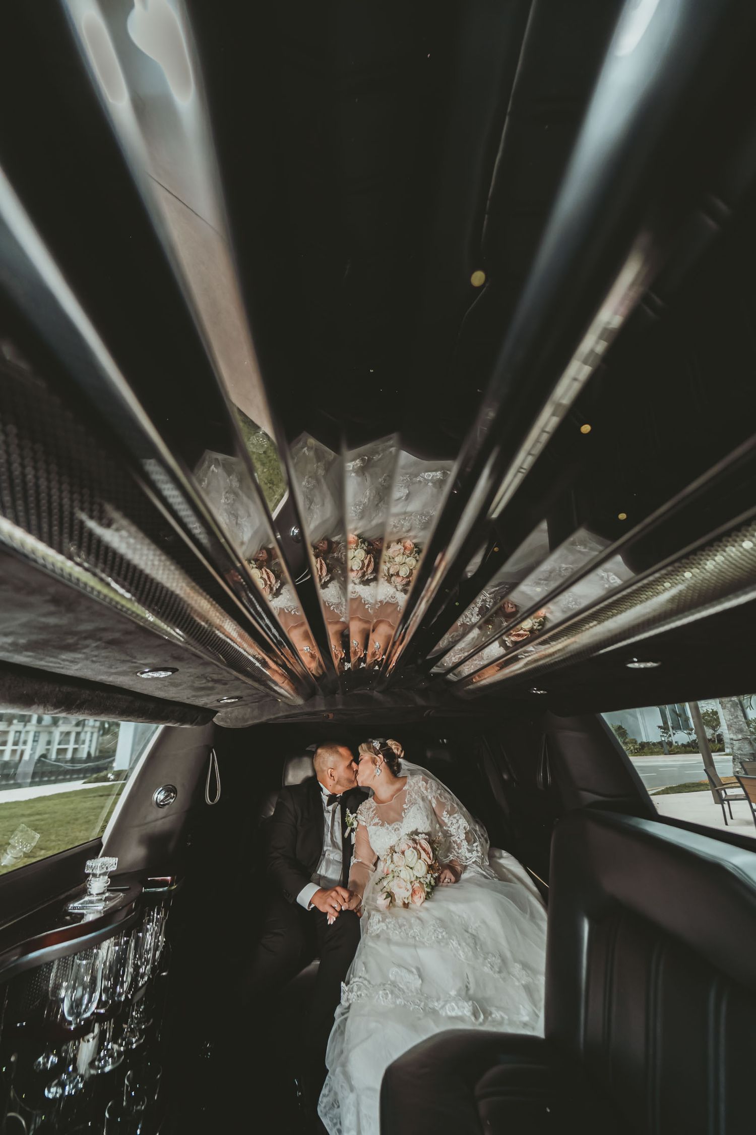 Novios se besan apasionadamente en asiento trasero de limusina; vista interior con techo reflectante. Boda.