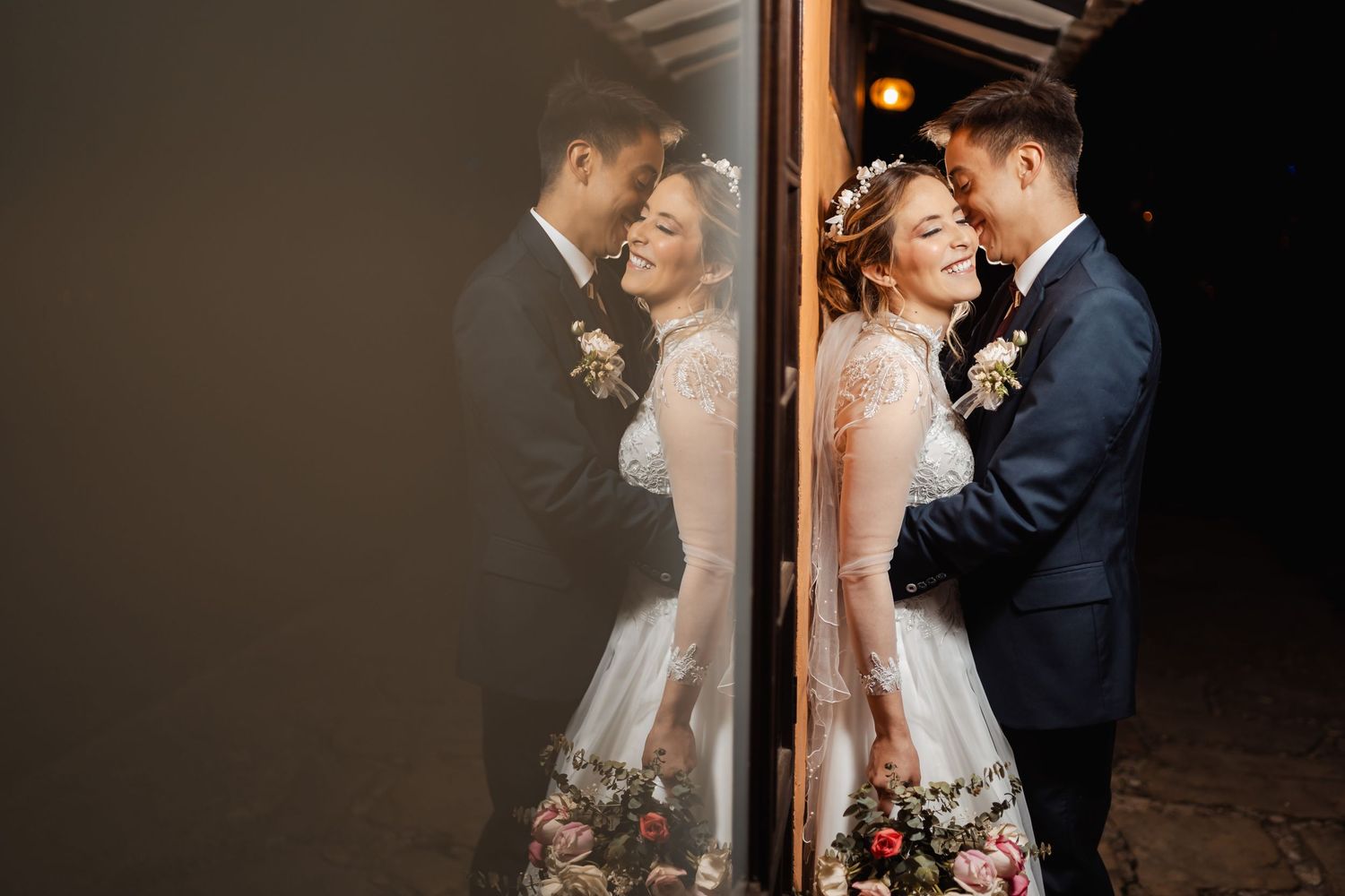 Novios riendo abrazados reflejados en ventana de noche; momento íntimo y feliz boda.
