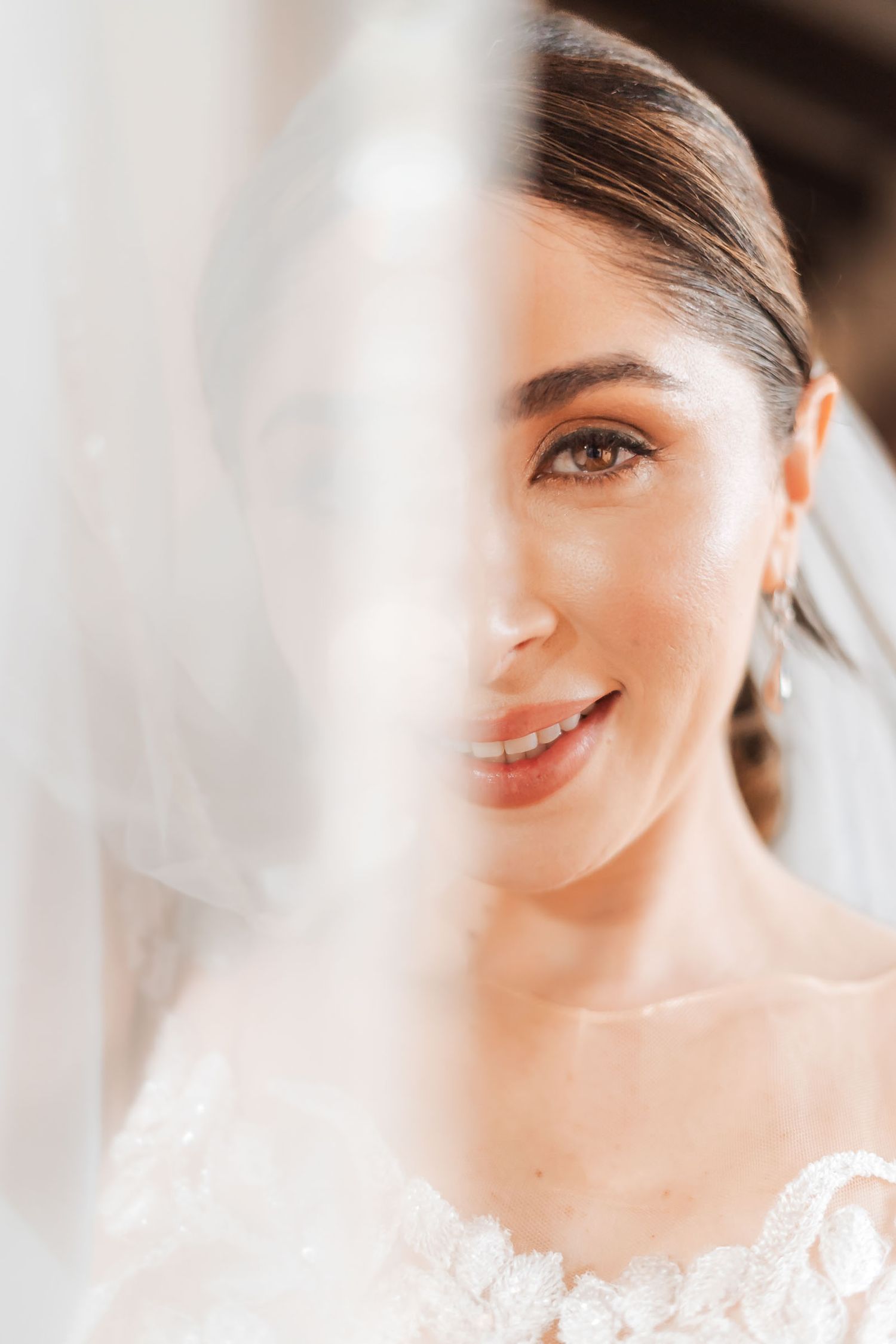 Retrato artístico primer plano: Rostro sonriente de novia parcialmente velado; maquillaje suave. Boda.