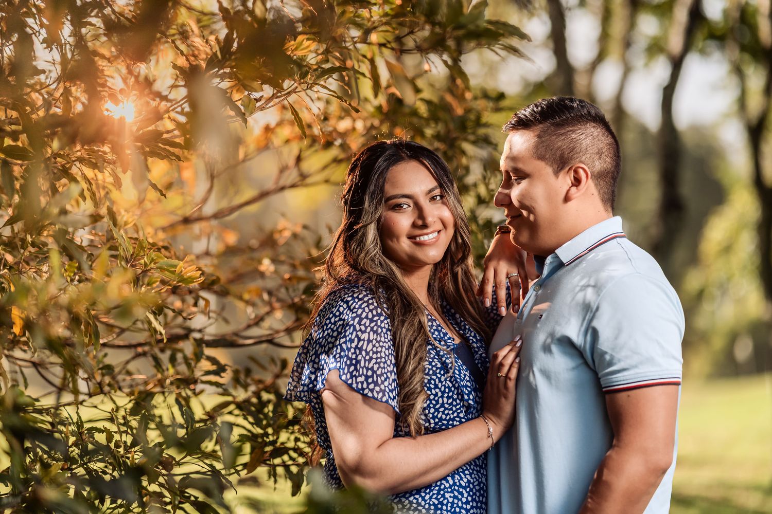 Pareja se abraza felizmente en exterior con luz cálida y destello detrás. Ella sonríe a cámara, él la mira con cariño. Romántica.