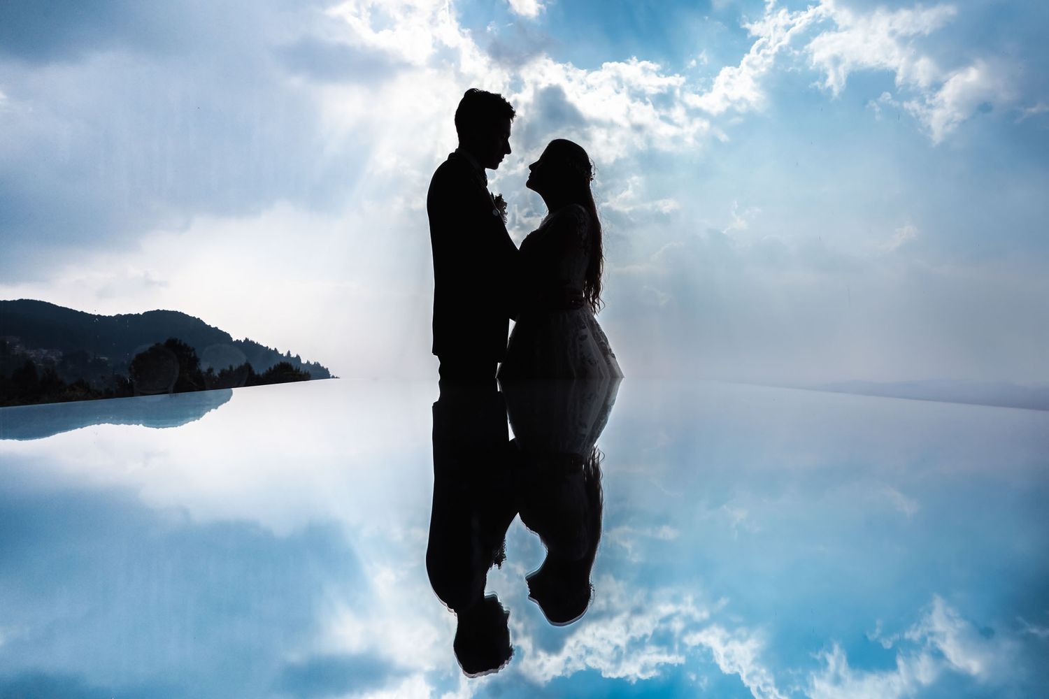 Novios creando silueta con reflejo perfecto en agua bajo cielo azul