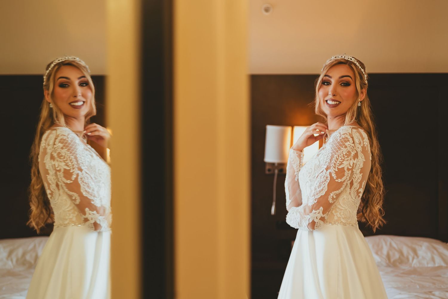 Novia sonriente con vestido de encaje y tocado de perlas posa frente a espejo, creando doble imagen.