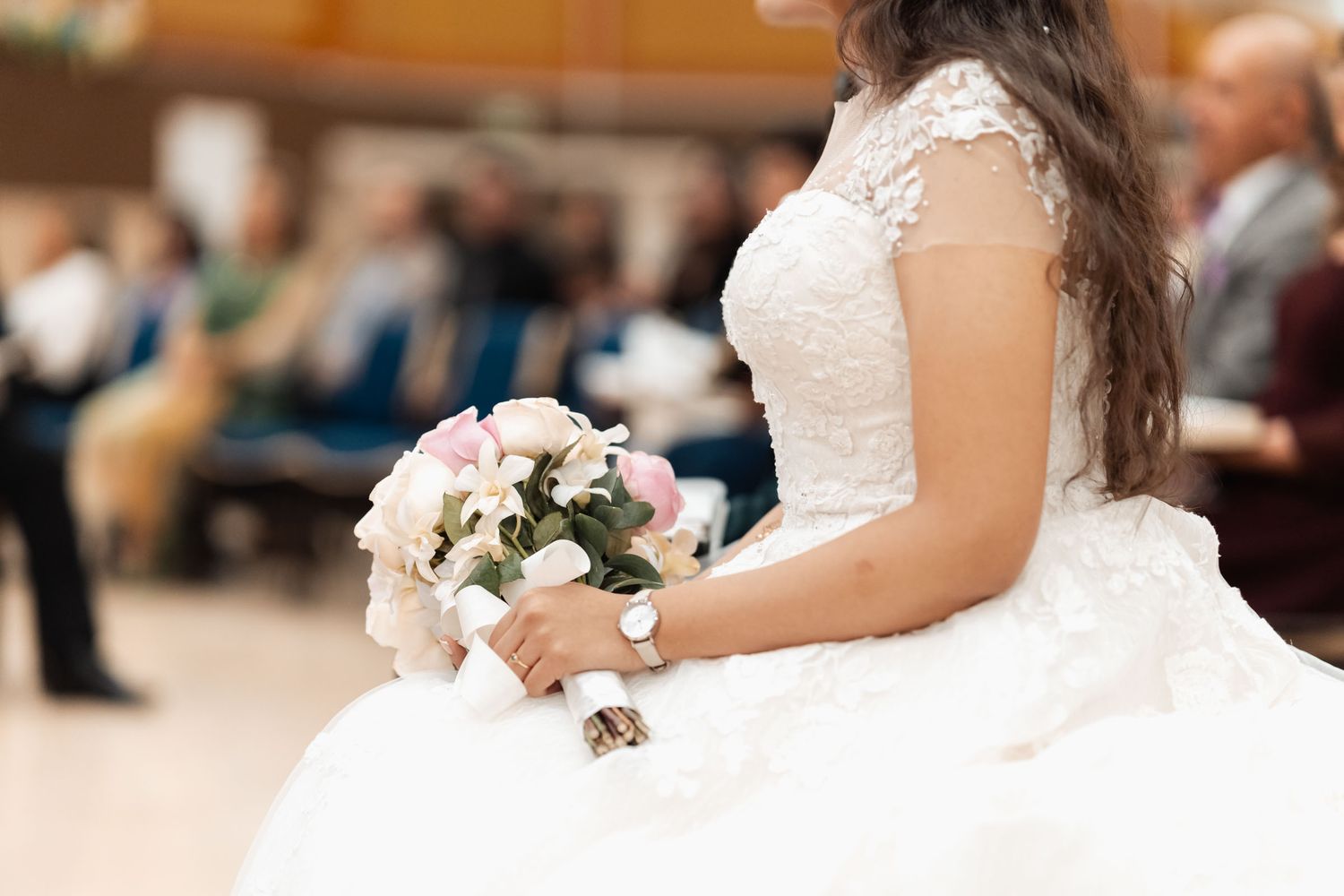 Novia sentada sosteniendo ramo de flores, detalle de vestido de boda