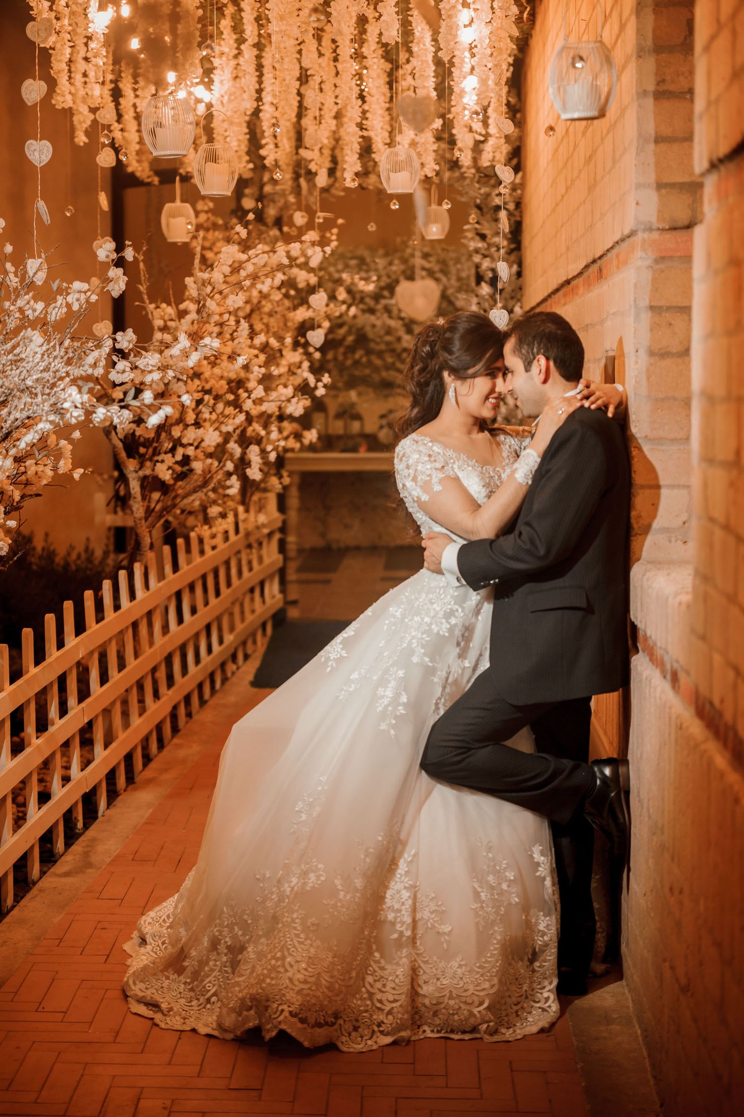 Romántica boda nocturna: pareja abrazada bajo árbol iluminado con luces cálidas y decoración bohemia. Ambiente íntimo y acogedor