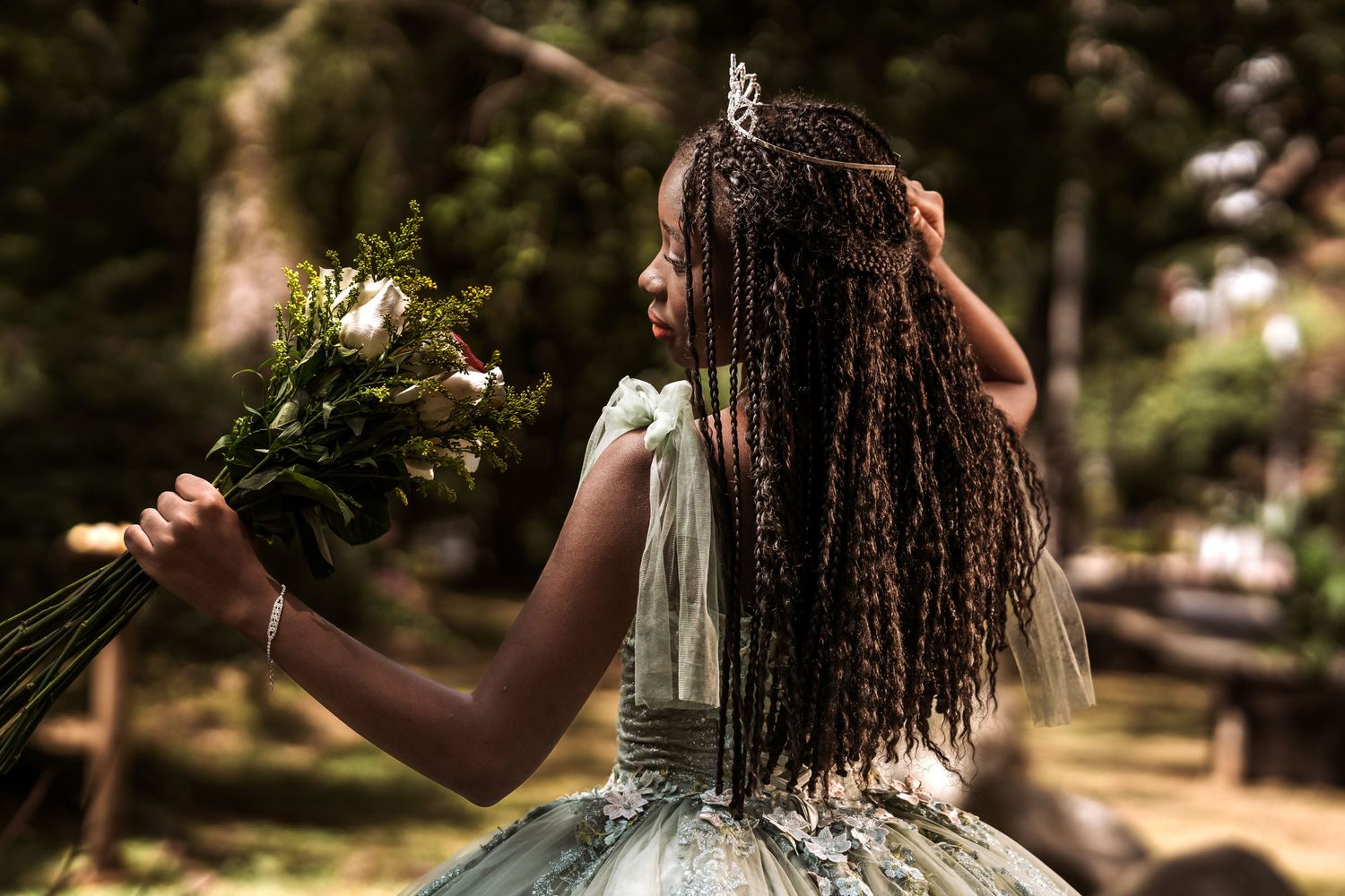 Joven afrodescendiente con trenzas, tiara y vestido princesa sostiene ramo; sesión quinceañera en bosque. Sesión de 15
