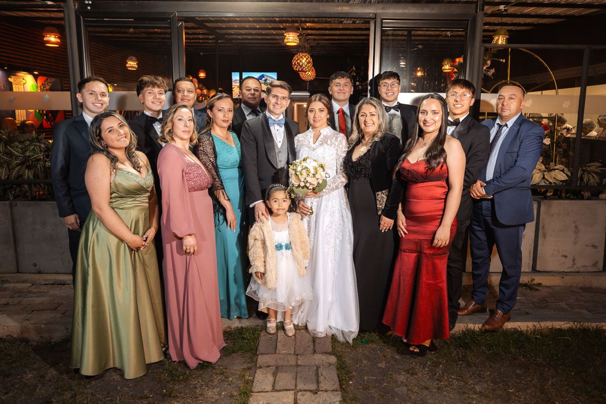 Grupo de boda posa feliz en exterior de noche. Novios con damas, caballeros y niña en foto grupal.