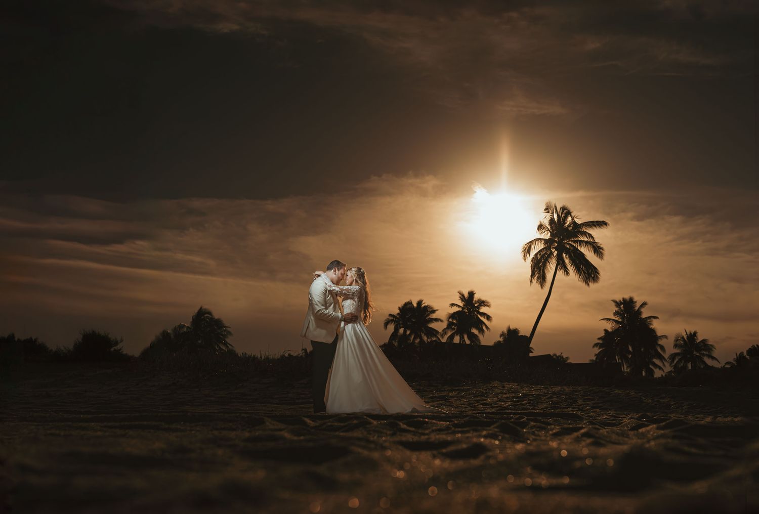 Novios se abrazan y besan apasionadamente en la playa con el sol y palmeras al atardecer. Boda romántica en Miami Florida.