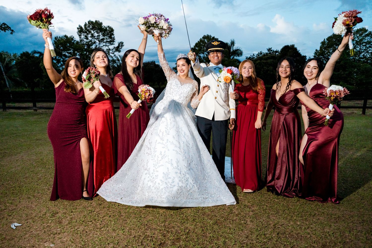 Los novios ríen junto a su cortejo de damas de honor vestidas de rojo en una foto de grupo