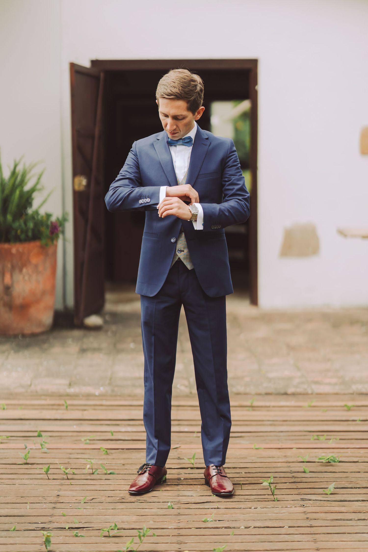 Novio con traje azul ajustándose los gemelos en el umbral de una puerta.