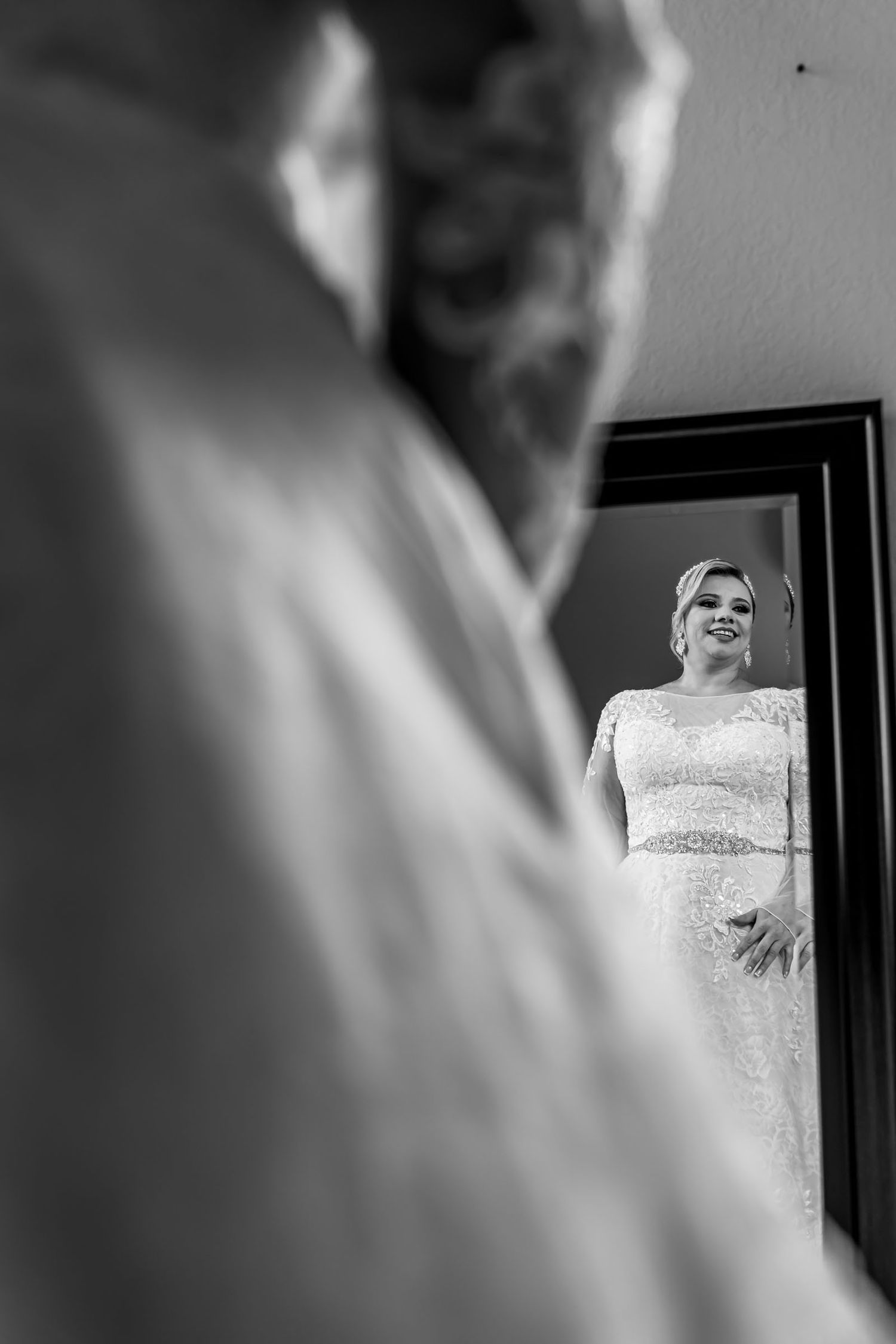 Foto B&W: Reflejo de novia en espejo vista sobre hombro; momento preparación boda.