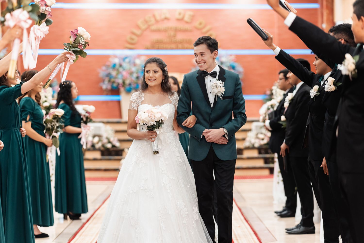 Novios en salida ceremonial bajo arco de biblias y flores en iglesia elegante.