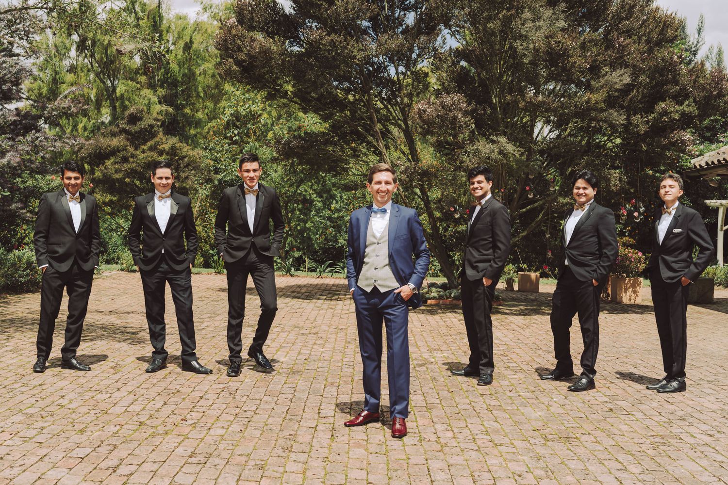 Novio con traje azul posando al aire libre con sus padrinos de boda.
