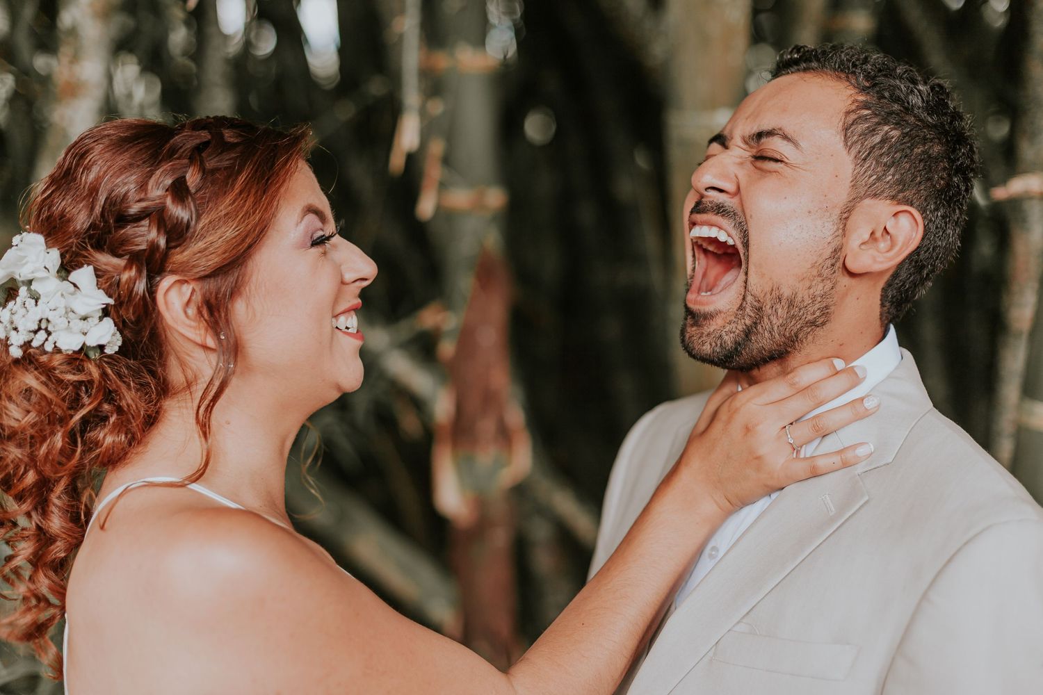 Novia juega a 'ahorcar' al novio mientras ambos ríen; foto divertida y espontánea de boda.