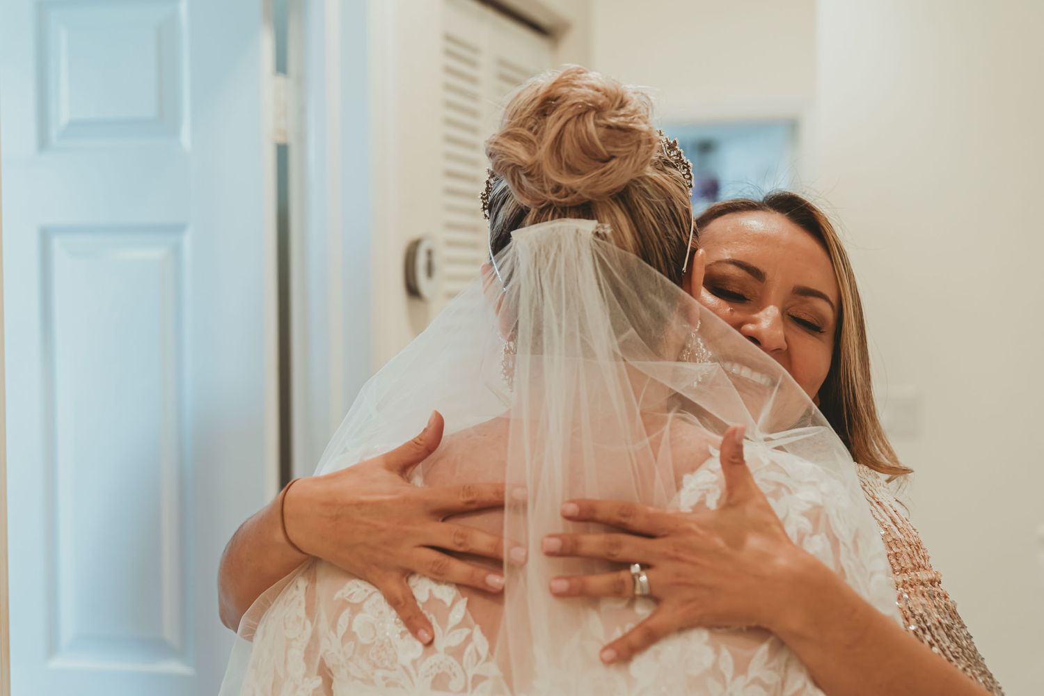 Novia (vista espalda) comparte abrazo tierno y emotivo con madre o dama de honor durante preparación boda.