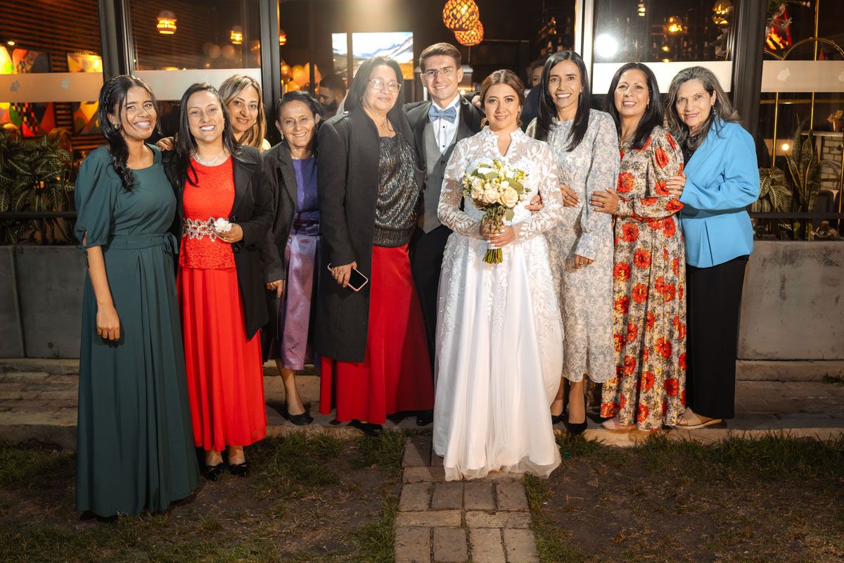 Grupo de boda posa feliz en exterior de noche frente a edificio iluminado. Novios con familia o amigos.