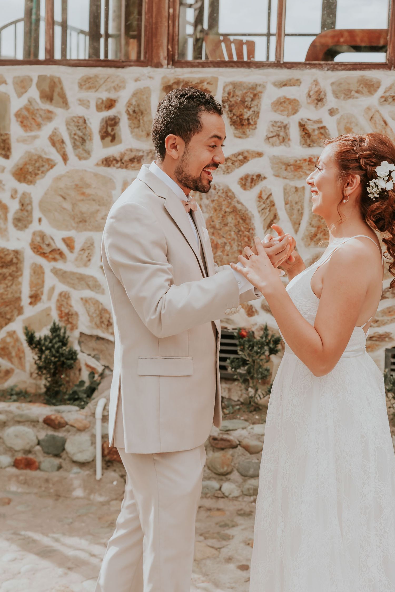 Novio con traje claro reacciona sonriente al ver a novia (vestido blanco) por primera vez. 'First look' boda.