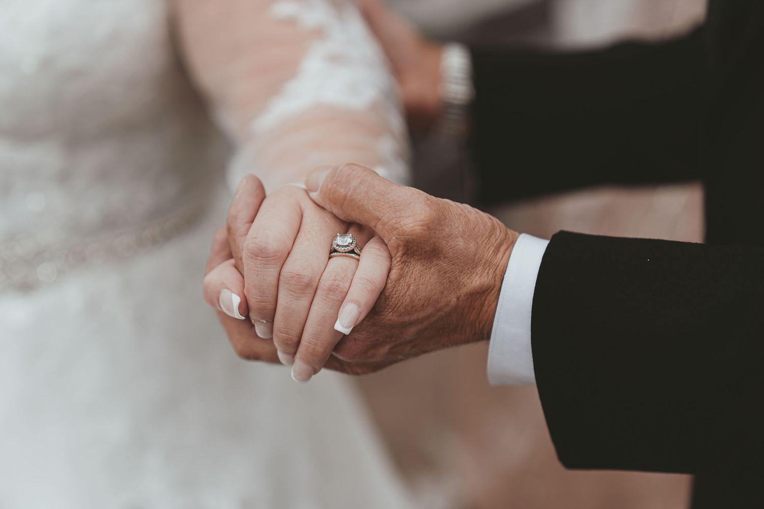Detalle boda manos entrelazadas: Novia con anillo compromiso sostiene mano de padre/familiar. Vínculo.