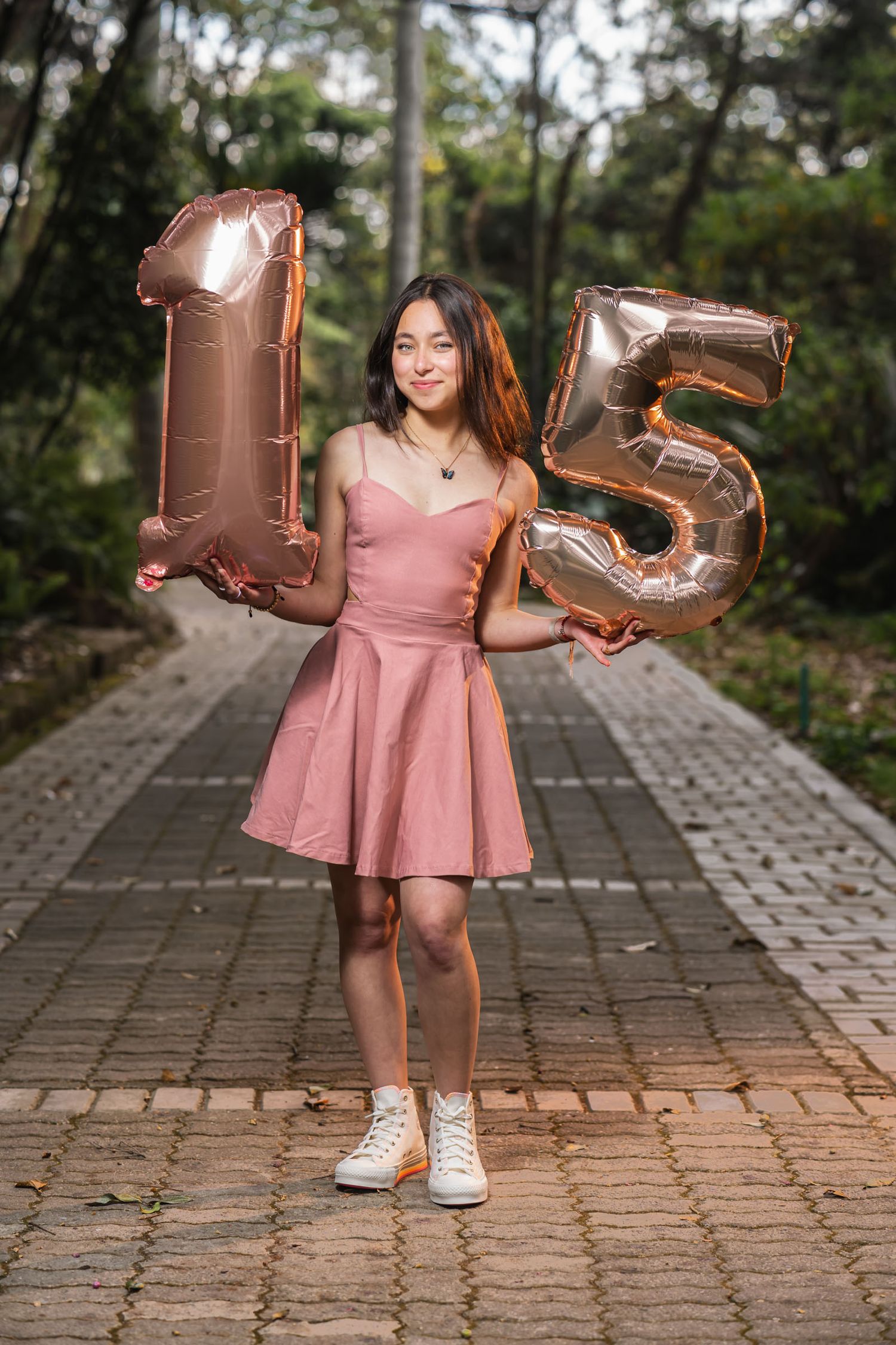 Joven quinceañera con vestido corto rosa y zapatillas blancas sostiene globos gigantes 