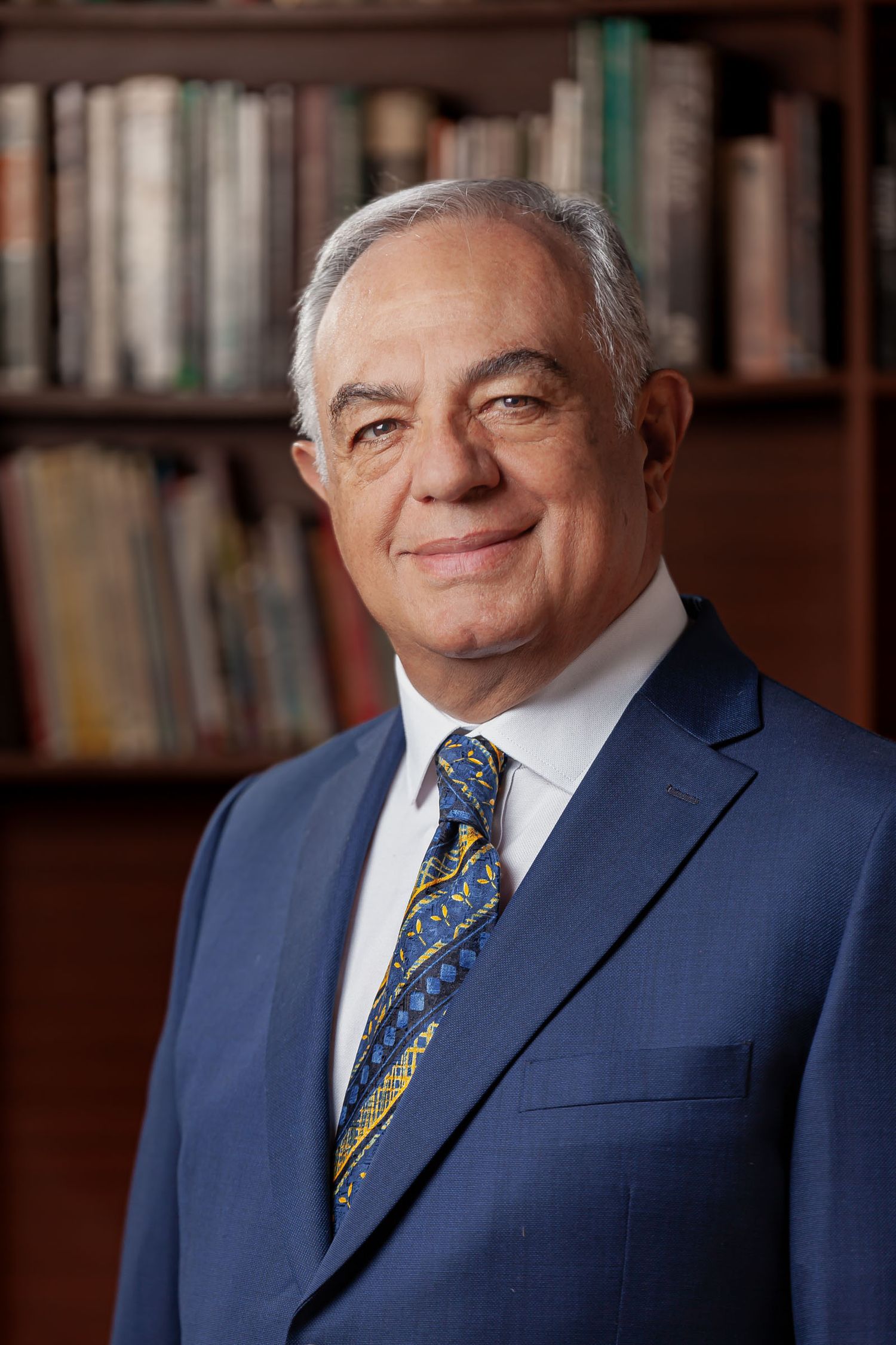Retrato profesional y corporativo de Luis Eduardo sonriendo a la cámara con una bibliotea de fondo