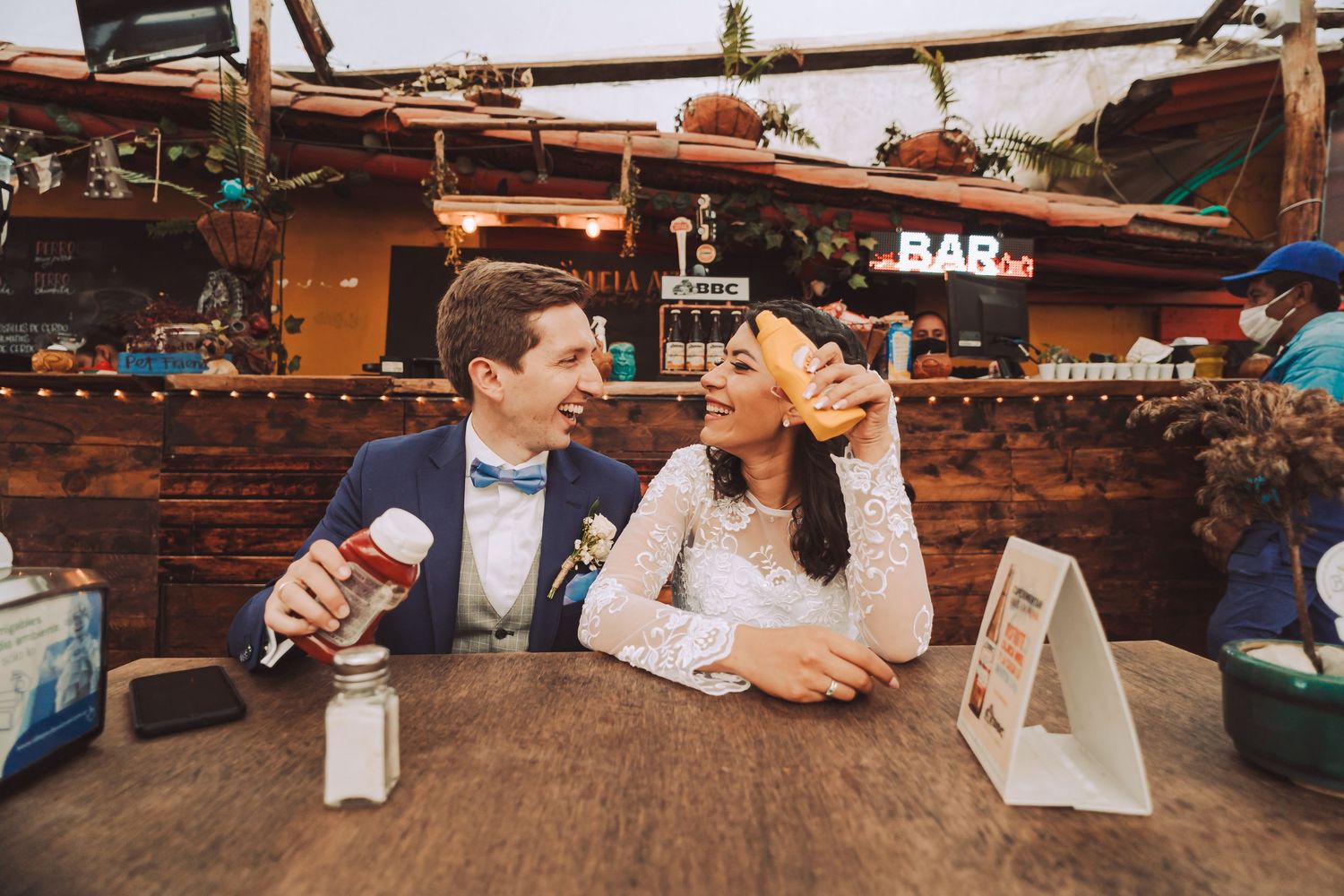 Foto de boda original: Novios se divierten comiendo y riendo en un restaurante, sosteniendo un hot dog y ketchup.