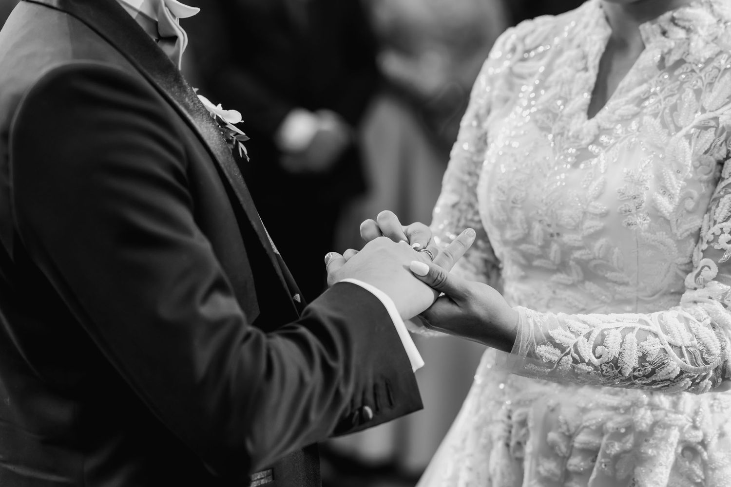 Primer plano blanco y negro de manos de novios unidas durante ceremonia, anillo visible. Símbolo de su unión.