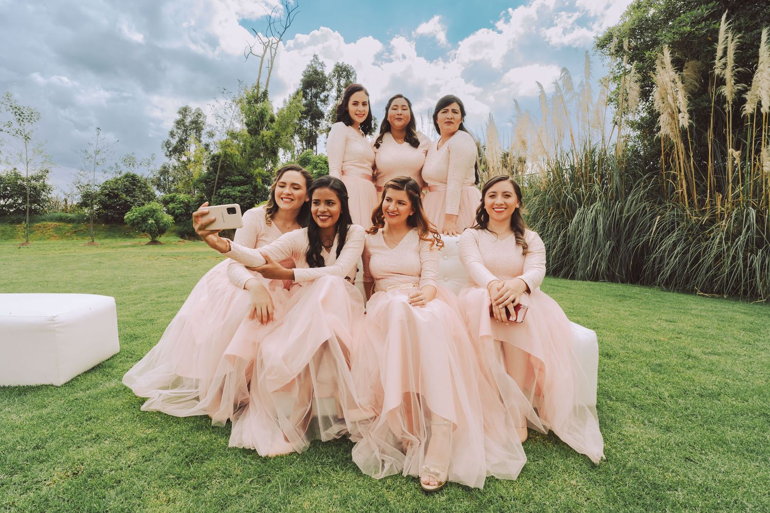 Novia sentada en el césped con sus damas de honor durante una sesión de fotos.