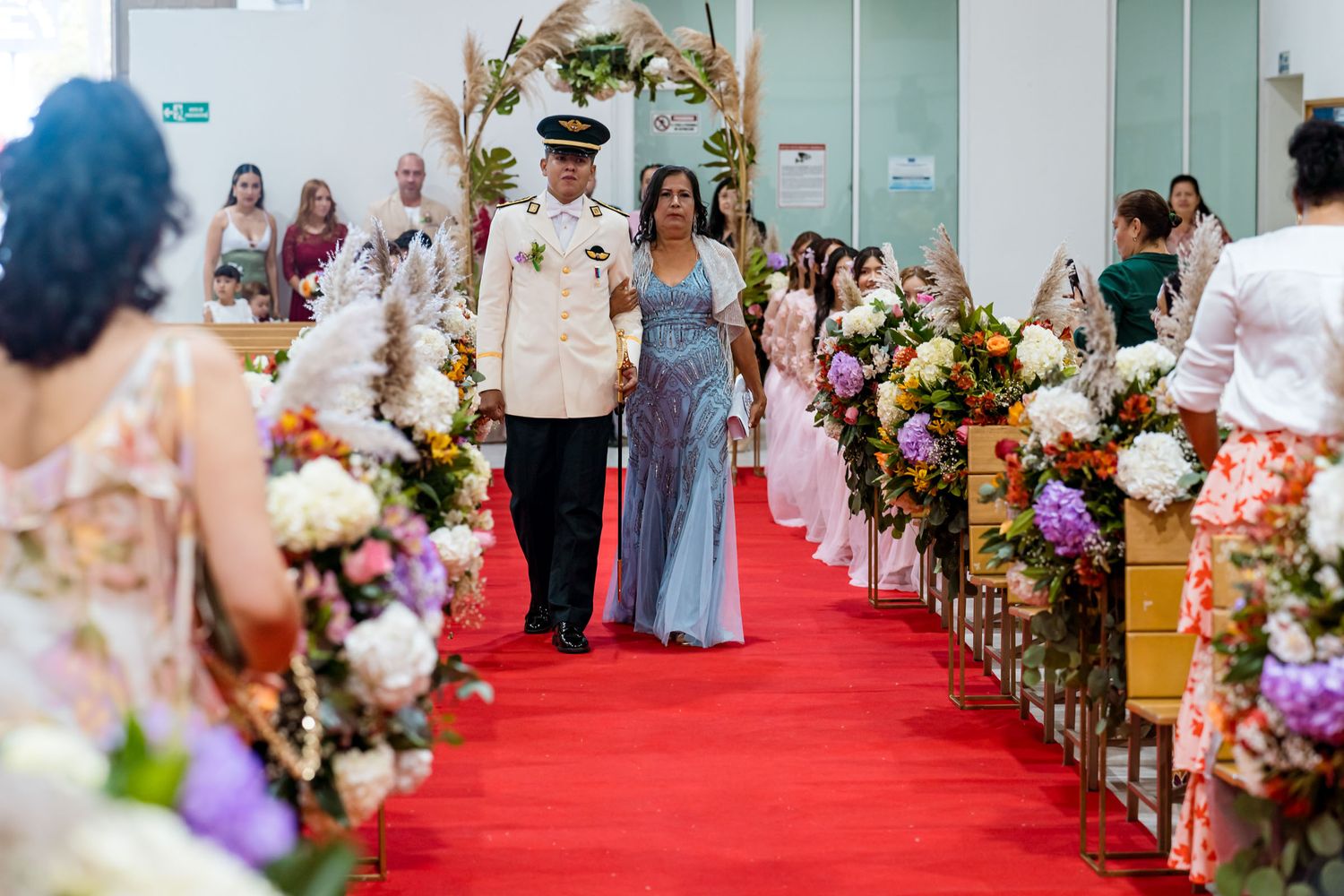 Novio con uniforme militar camina de la mano con su madre por el pasillo de la iglesia en su boda en Villavicencio