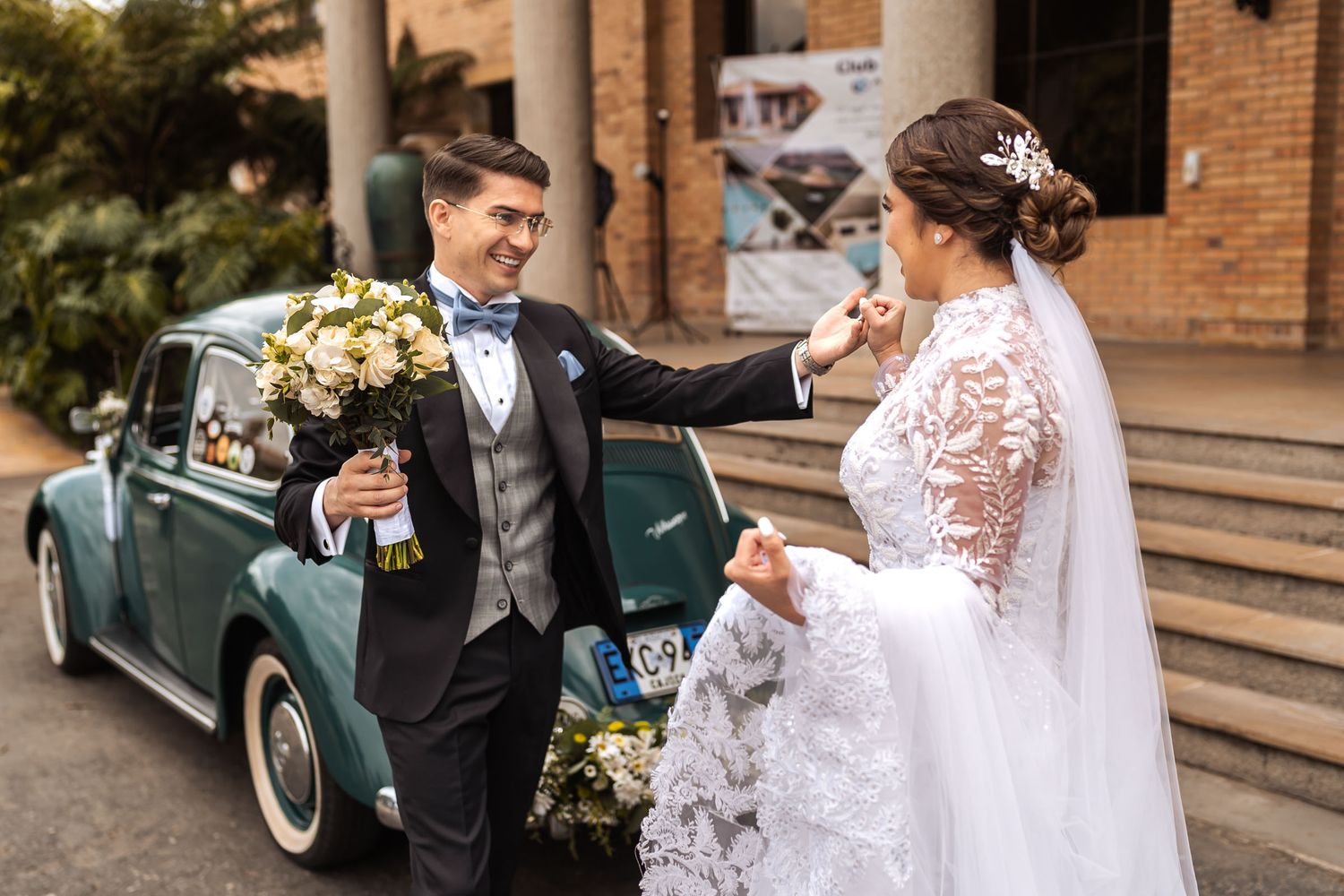 Novio sonriente sostiene ramo y mano de la novia junto a coche clásico VW Escarabajo verde decorado; fotografía de boda.