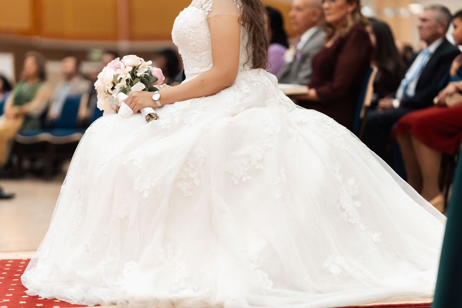 Novia sentada frente al altar, vista lateral del vestido con cola larga