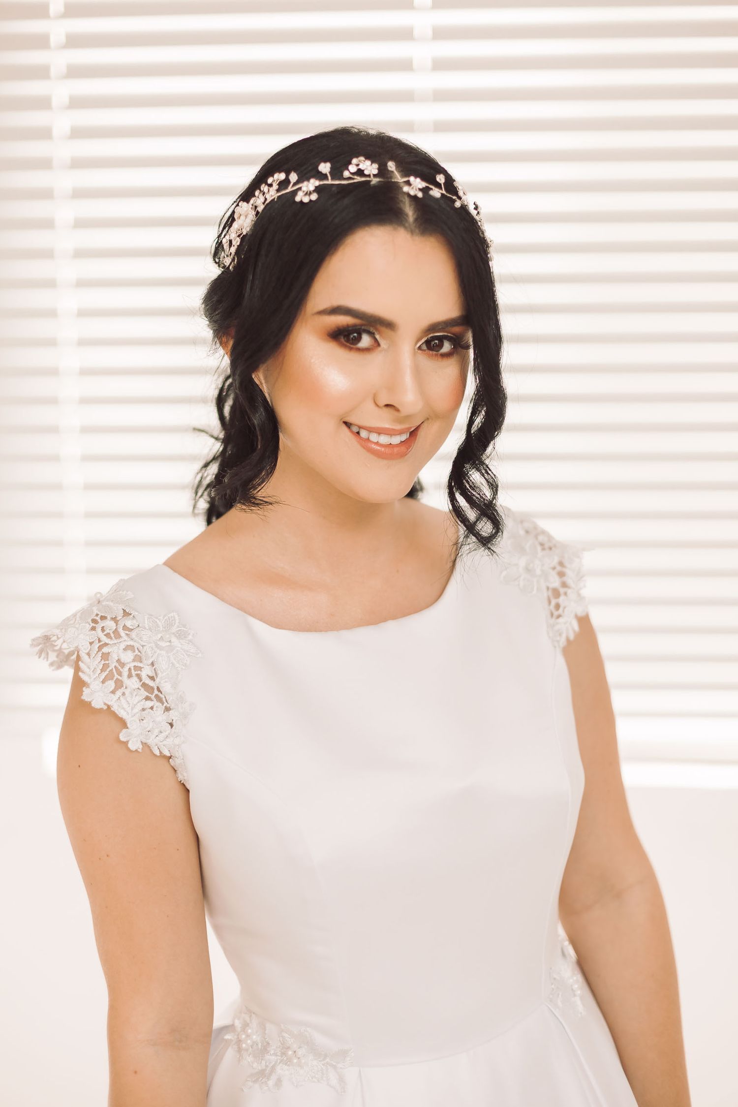 Primer plano de novia sonriendo con vestido blanco y tocado floral. Retrato de boda feliz con fondo suave.