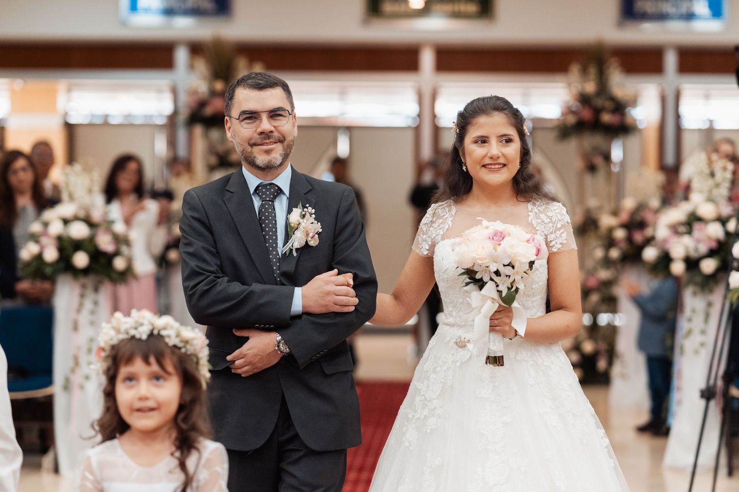 Padre camina de la mano con la novia sonrientes junto a pajecita durante celebración de boda