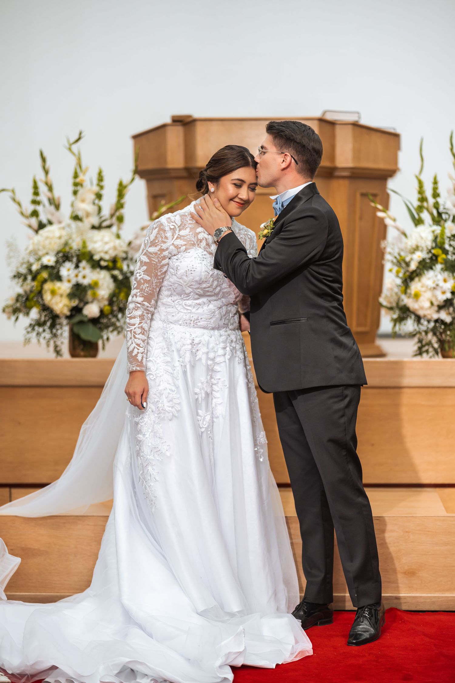 Novios se besan en la frente frente al altar durante su ceremonia de boda. Momento tierno e íntimo. Boda IDMJI