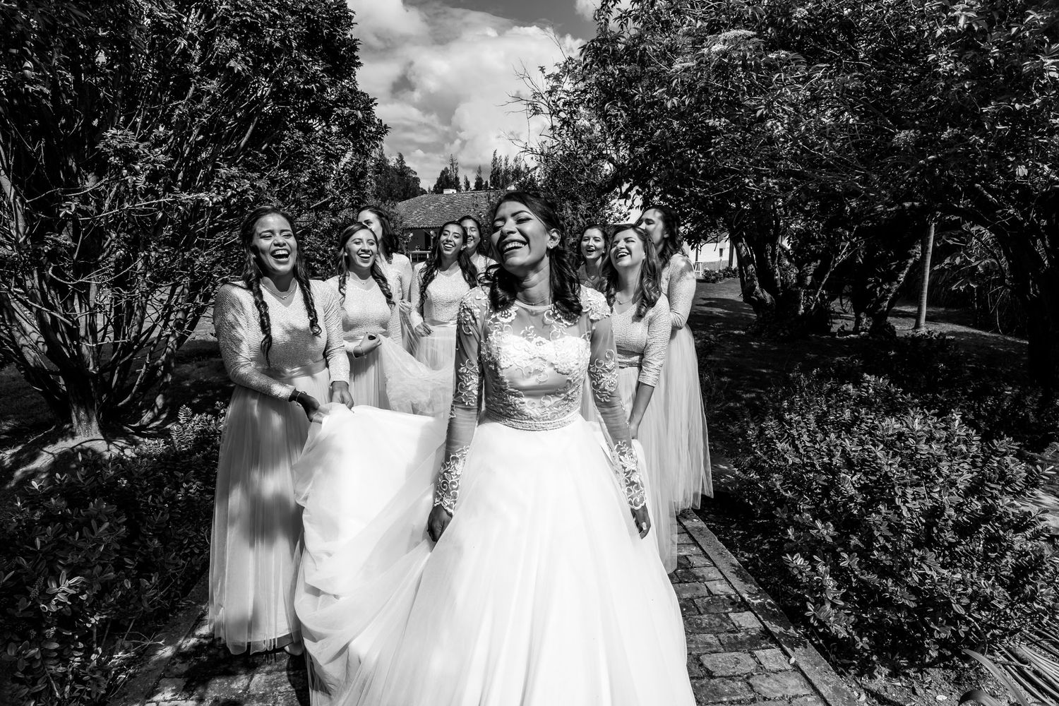 Novia caminando con sus damas de honor en un jardín, foto en blanco y negro.