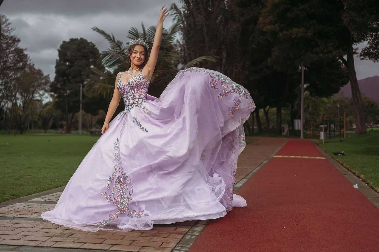 Quinceañera celebra con vestido lavanda princesa y tiara en alfombra roja exterior; falda en movimiento.