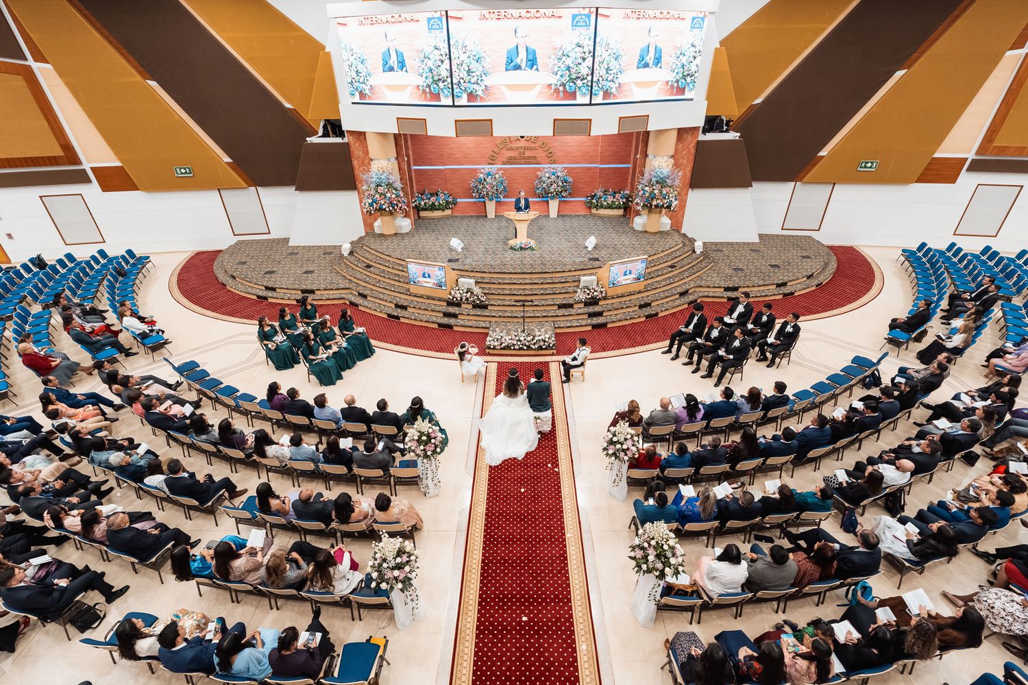 Vista aérea de boda en iglesia: Novios caminan por largo pasillo rojo entre invitados sentados. Ceremonia nupcial en boda IDMJI.