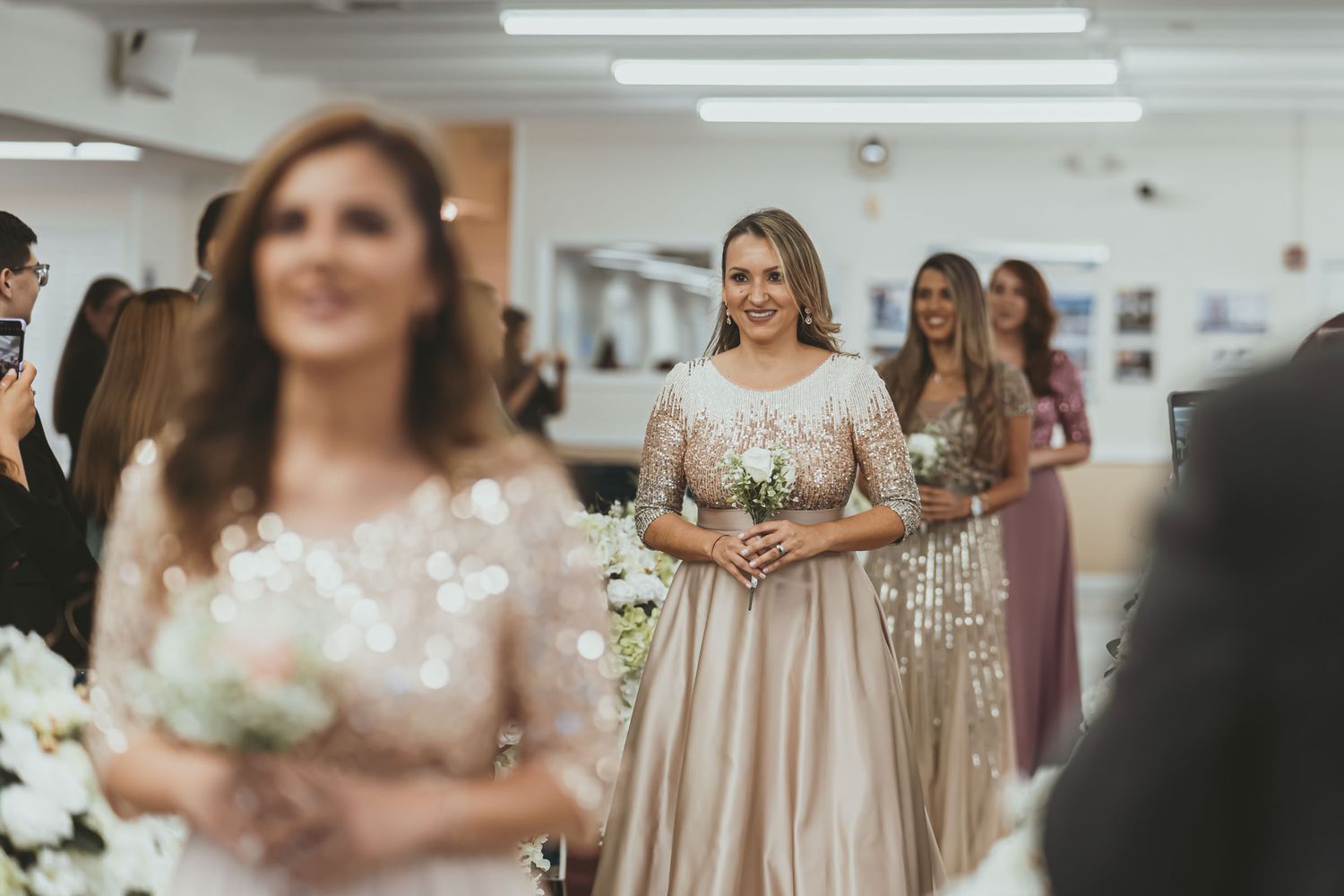 Damas de honor sonrientes caminan por pasillo iglesia en procesión boda; vestidos largos elegantes.