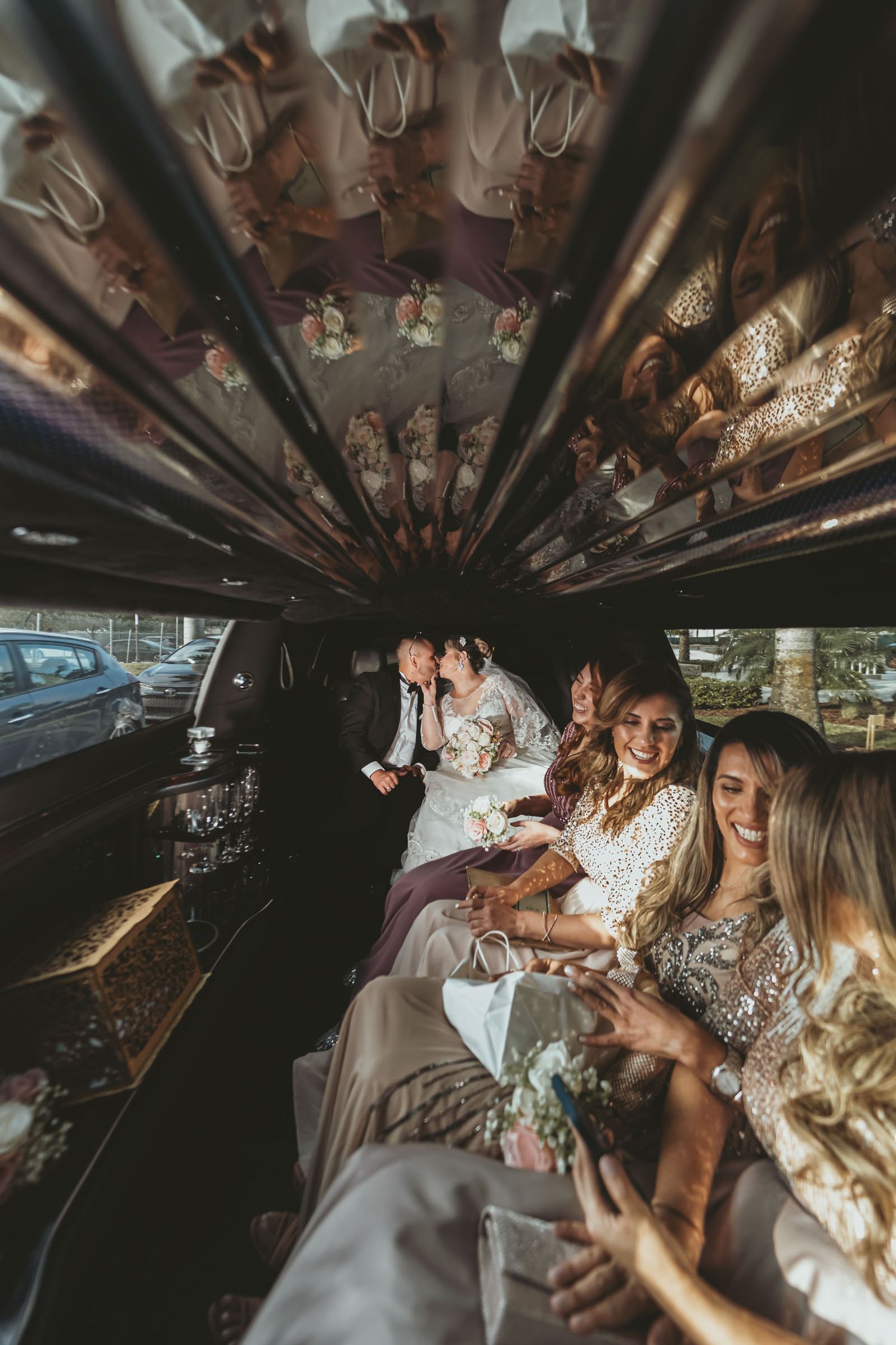 Novios, damas de honor y amigos celebran dentro de limusina; vista interior con techo reflectante. Fiesta boda.