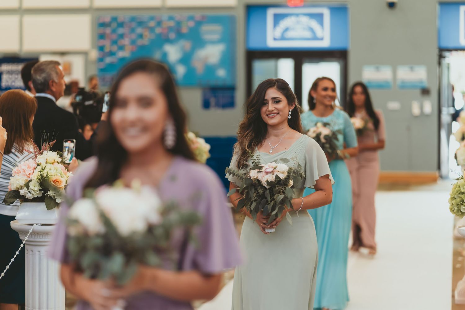 Damas de honor con vestidos color pastel y ramos caminan por pasillo iglesia en procesión boda.