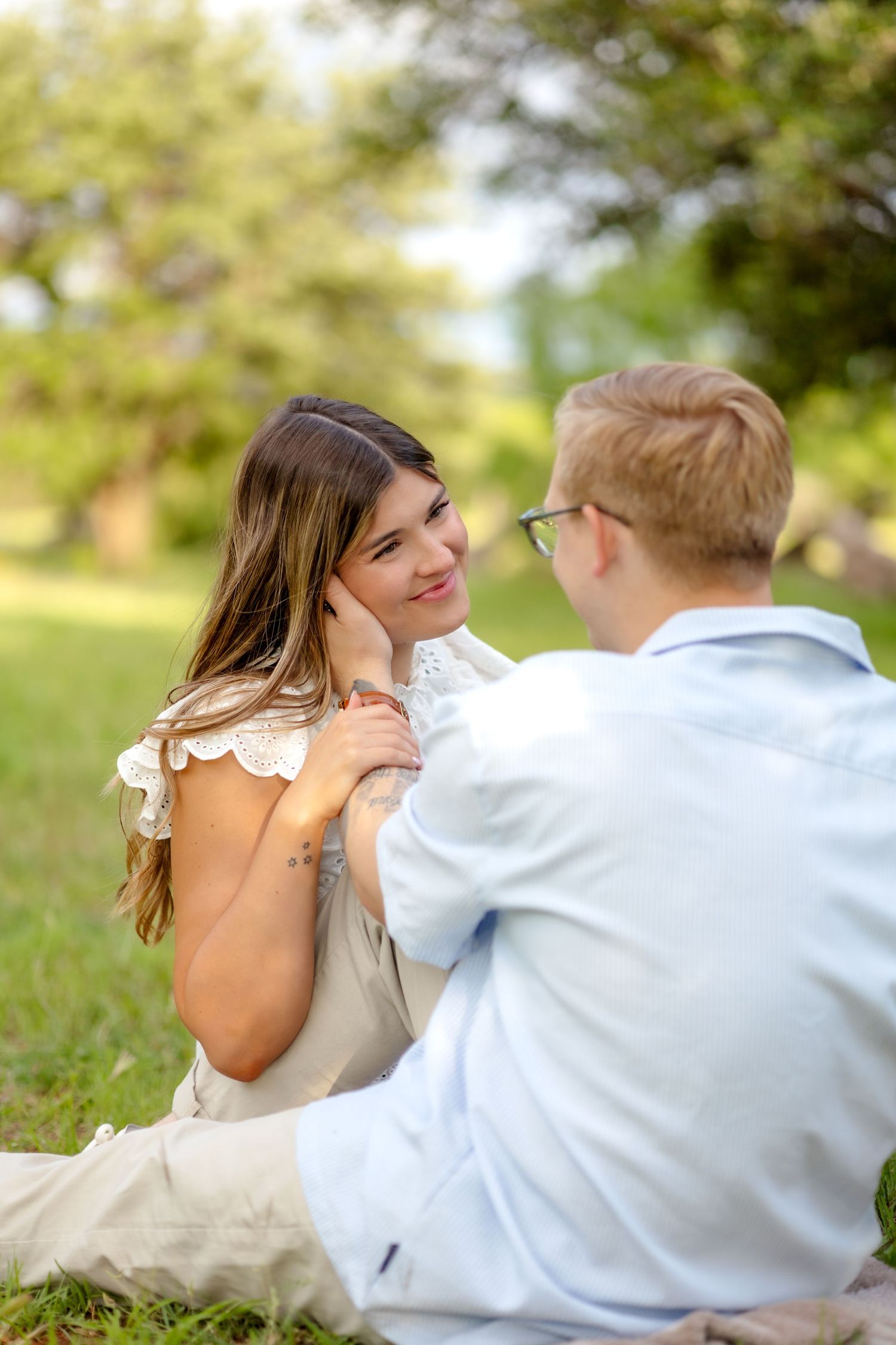 husband and wife sitting facing each other in a field and admiring one another during couple's photo session in Abilene, Texas
