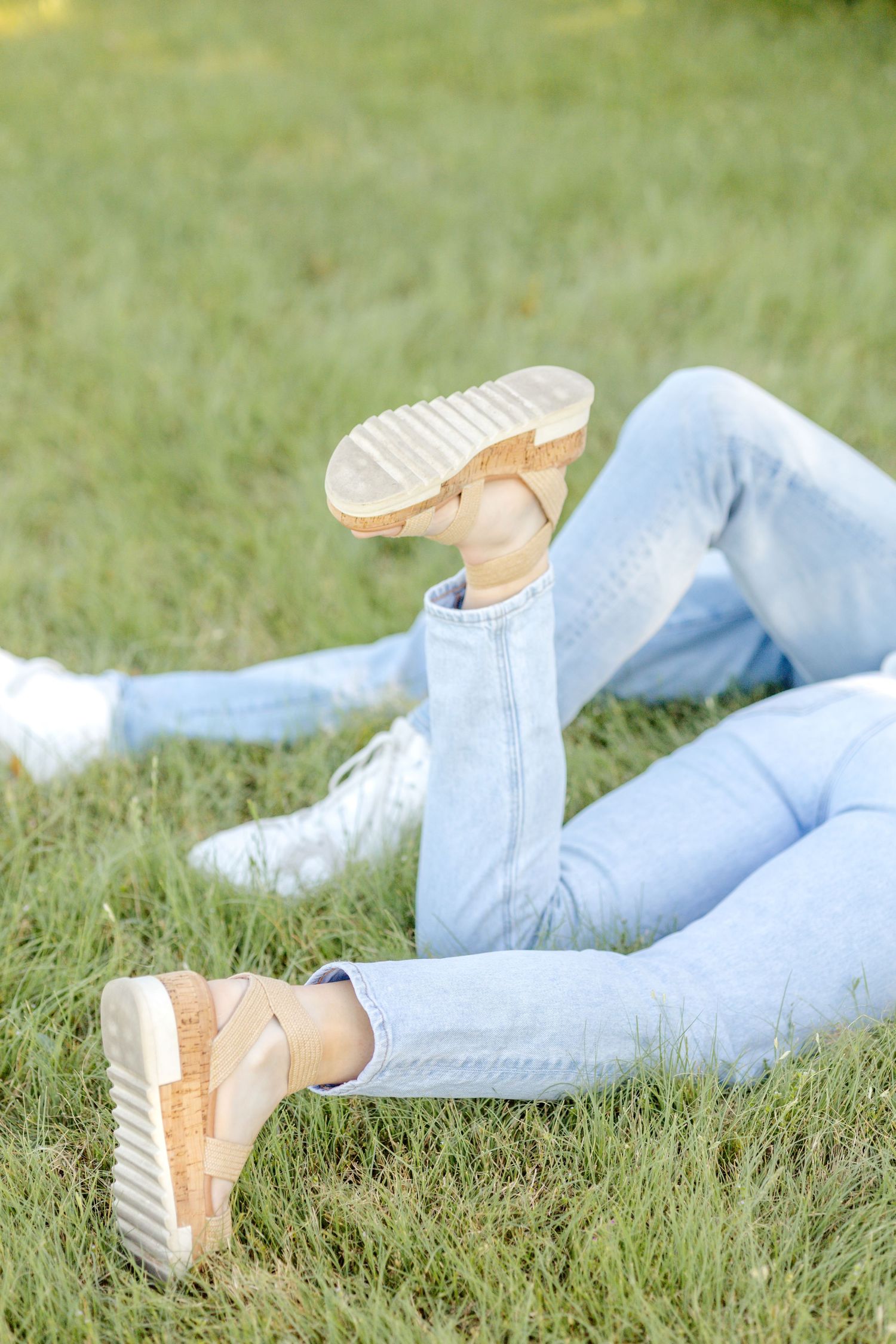 Detail image of an engaged couple's feet kicking around while laying in the grass at a field at White Rock Lake during engagement photos