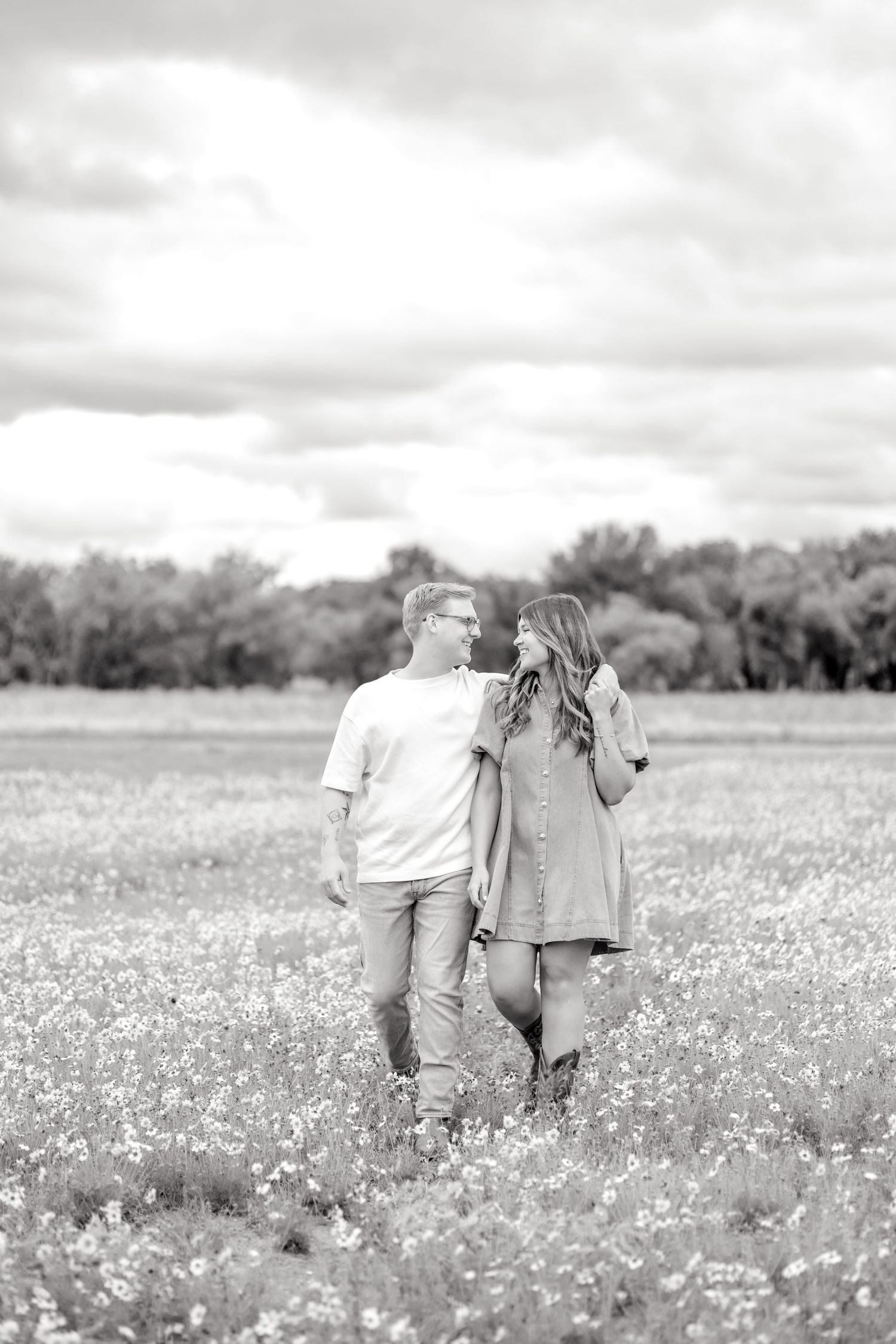 Black and white image of married couple walking through a wildflower field in Abilene, Texas and smiling at one another at couple's session