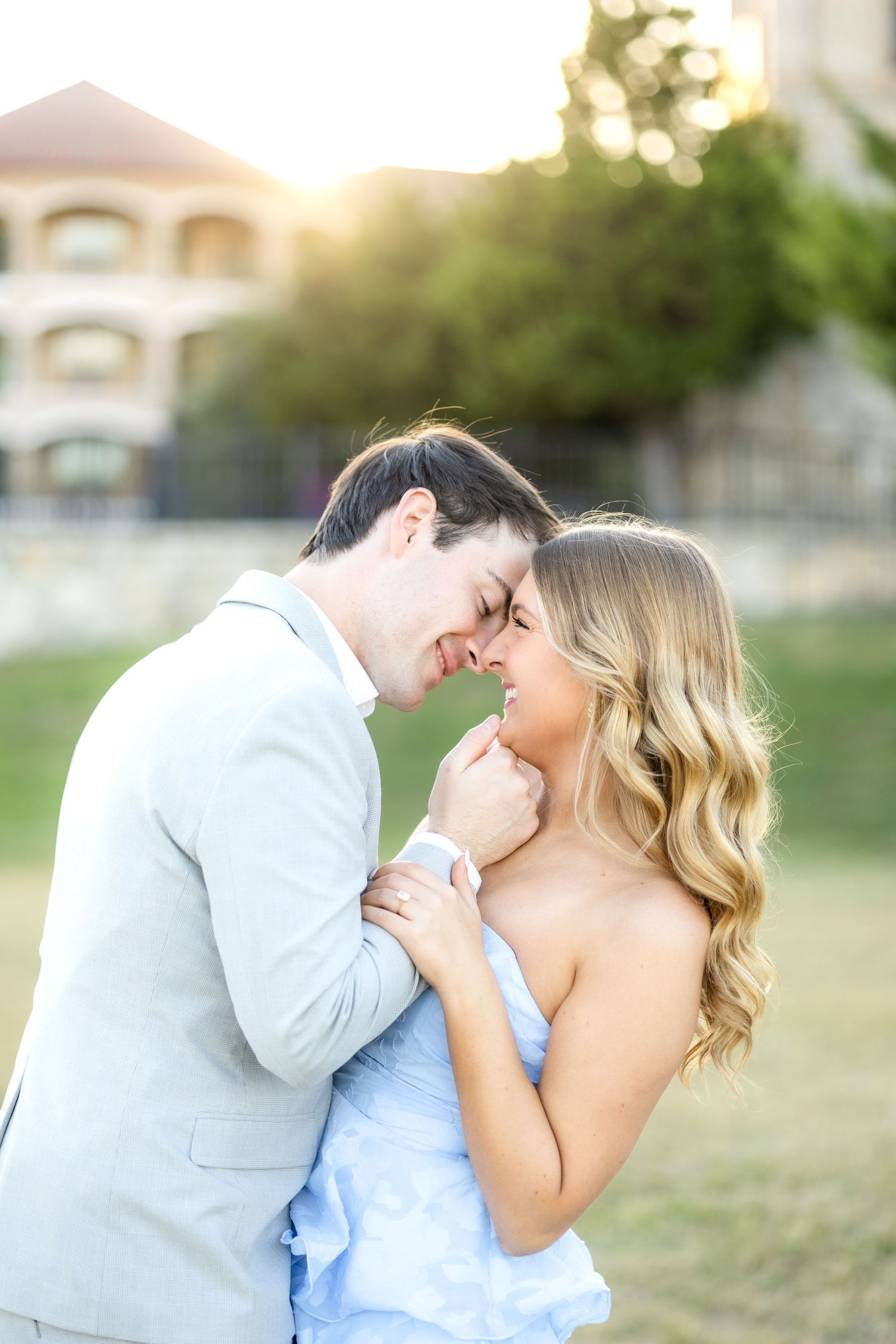 Engaged couple going in for kiss in a light grey suit and blue dress at Adriatica Village engagement session