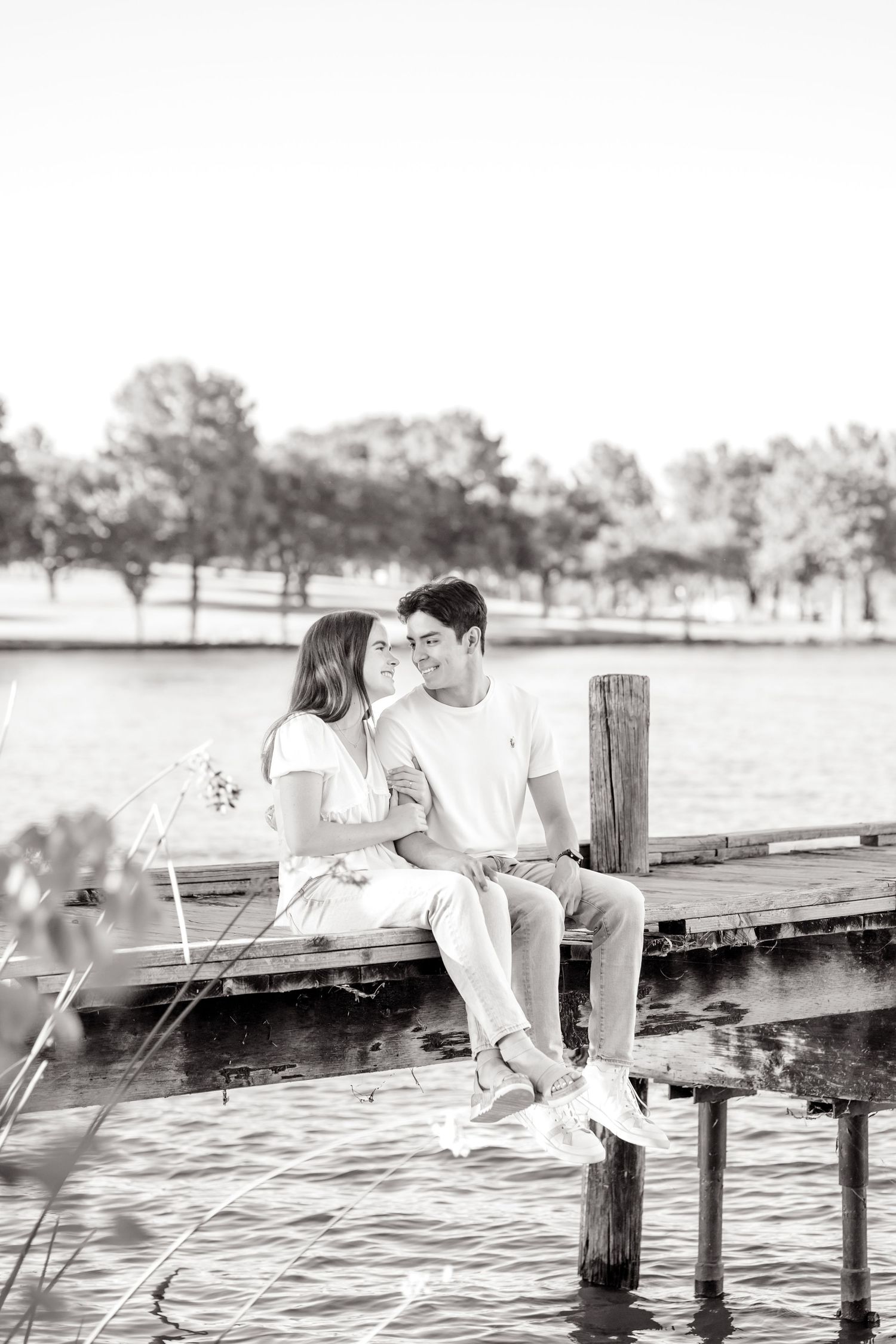 Engaged couple sitting on the dock at White Rock Lake in Dallas and looking sweetly into each other's eyes