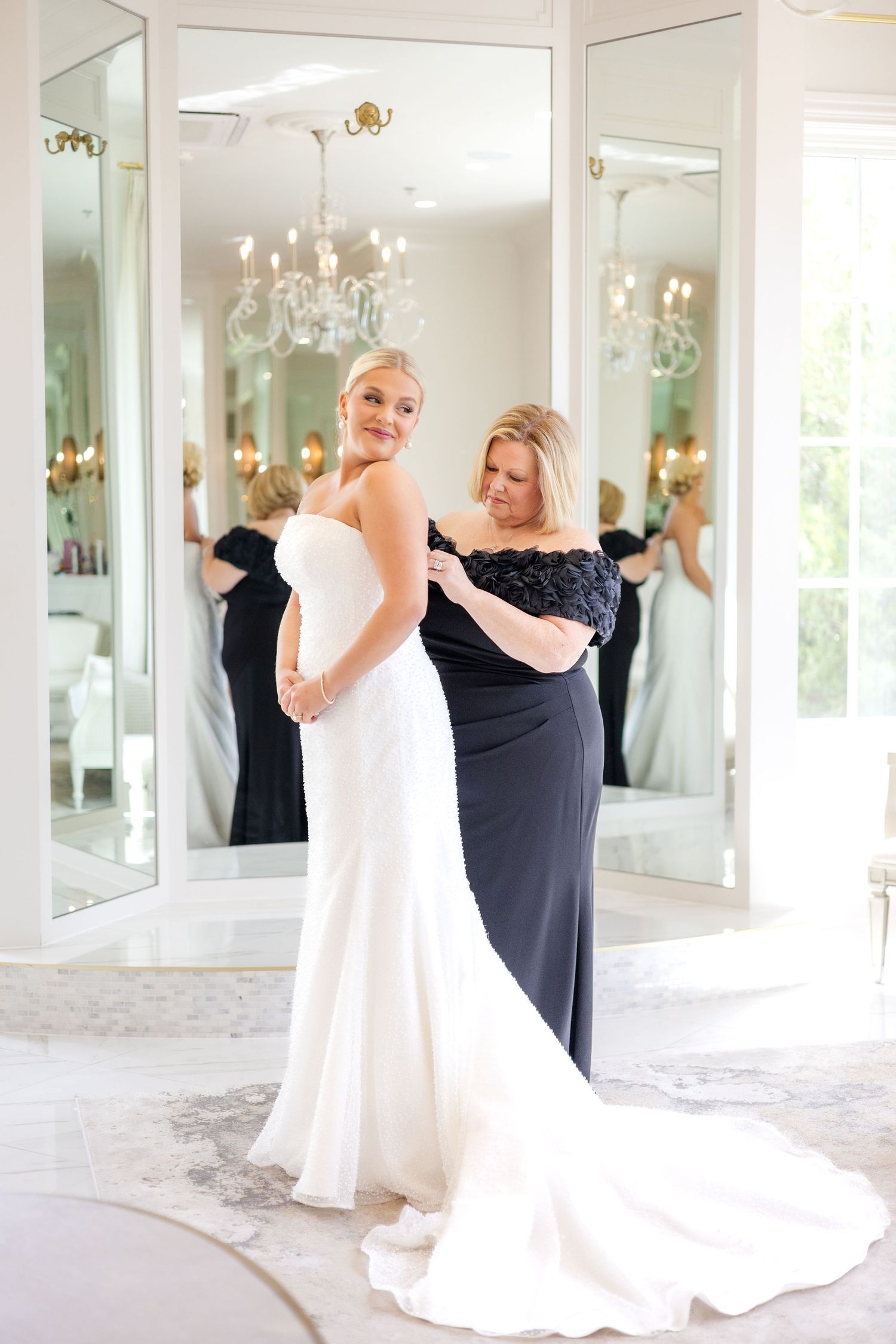 Mother of the bride helping the bride button her wedding dress as the bride smiles in the bridal suite at Dallas wedding