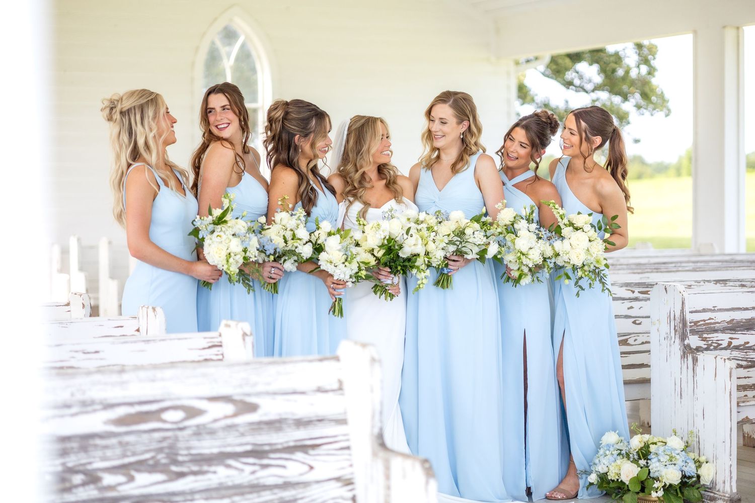 Bride and bridesmaids smiling at one another and holding Spring wedding bouquets in an open air wedding chapel near Dallas, Texas